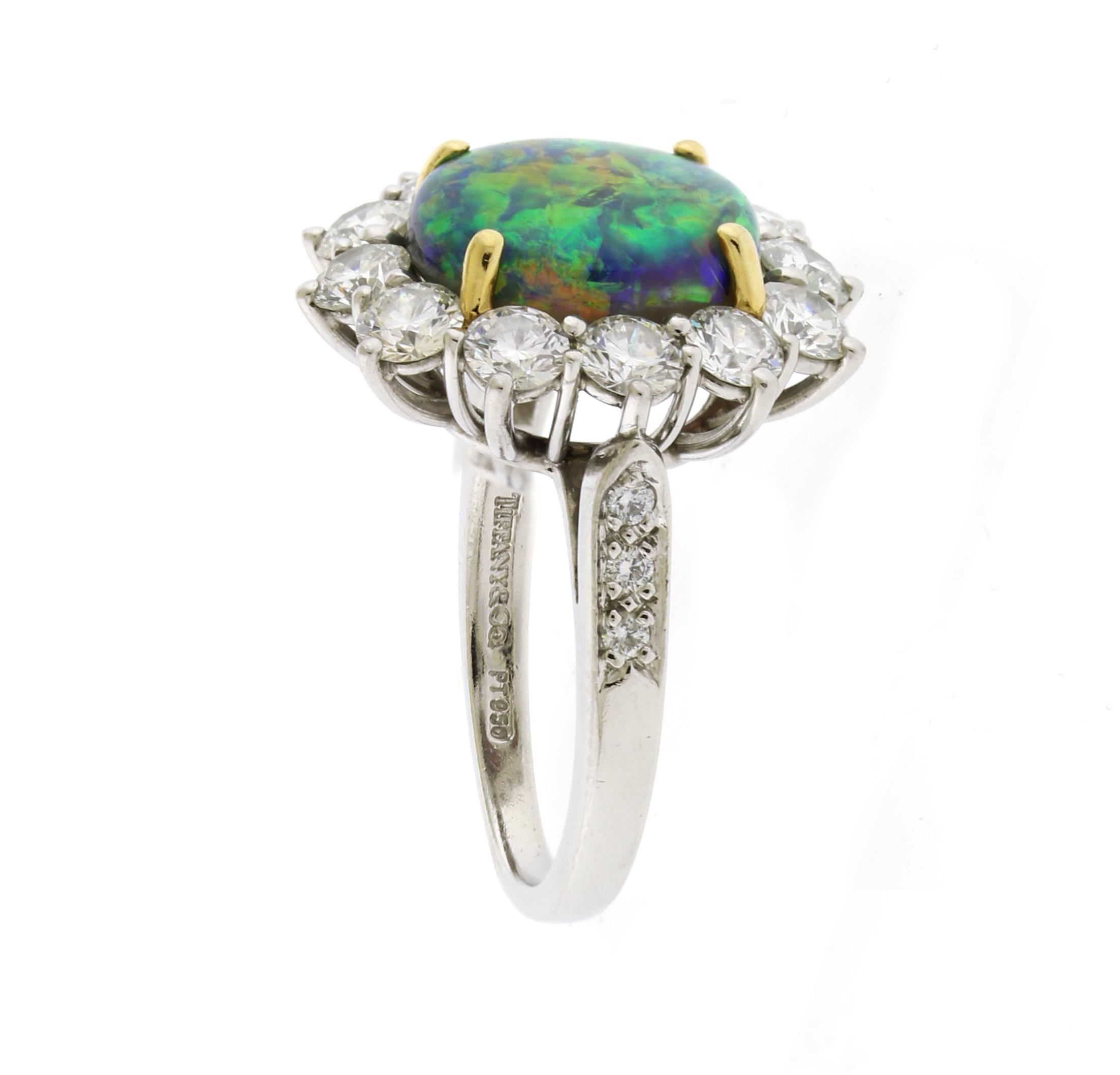 The Tiffany & Co. Black Opal and Diamond Ring features a stunning 4-carat gem black opal at its center, showcasing a vibrant play of color. It is beautifully accented by 12 round diamonds totaling approximately 3 carats. Crafted in platinum, the
