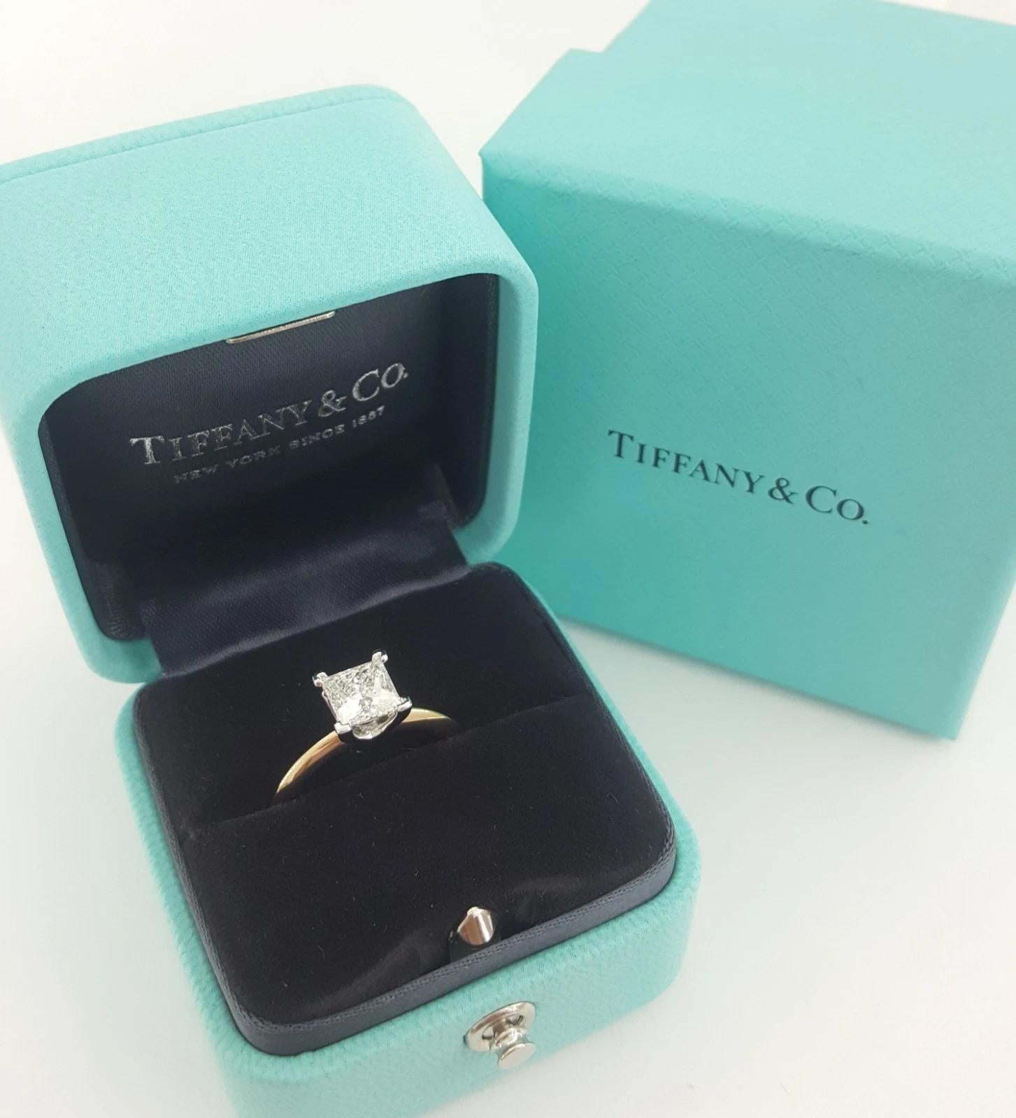 Un anillo de compromiso solitario atemporal e icónico de Tiffany & Co. con un impresionante diamante de talla princesa (cuadrado modificado brillante) de 1,08 quilates, graduado en color G y claridad VS1. Esta piedra excepcional tiene una talla