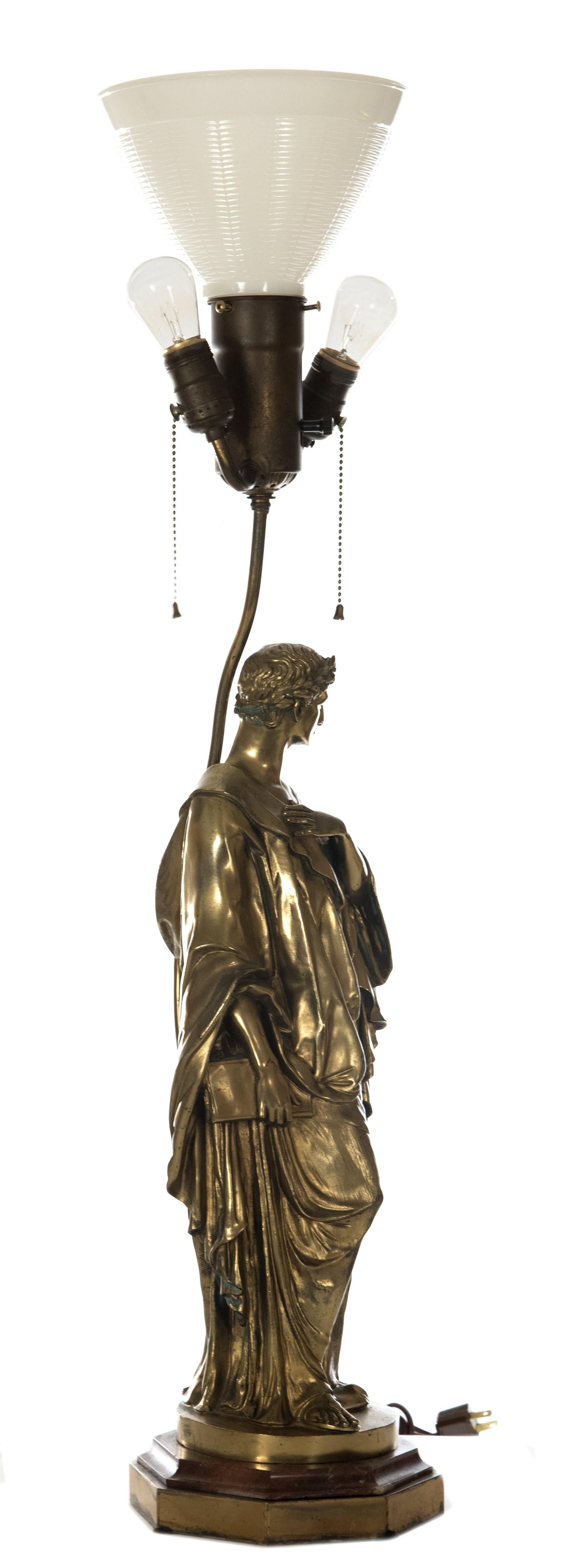 A bronze gilt-painted, three-light figural table lamp from Tiffany & Co., the stem supported by a Romanesque robed scholar holding a book, their head set with a crown of laurels, all on a round base that is stamped with 