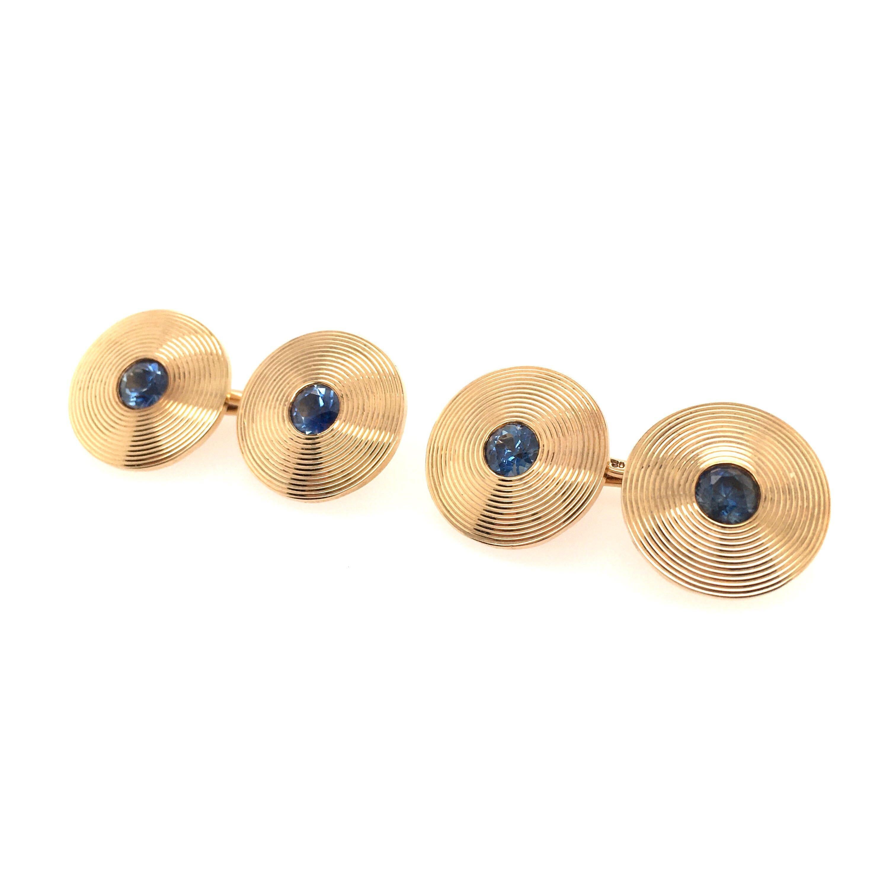 A 14 karat yellow gold and sapphire dress set. Tiffany & Co. Circa 1940.  Comprising a pair of cufflinks, each double link designed as ridged disc, centering an old cut sapphire, and three (3) shirt studs en suite.  Cufflink length is approximately