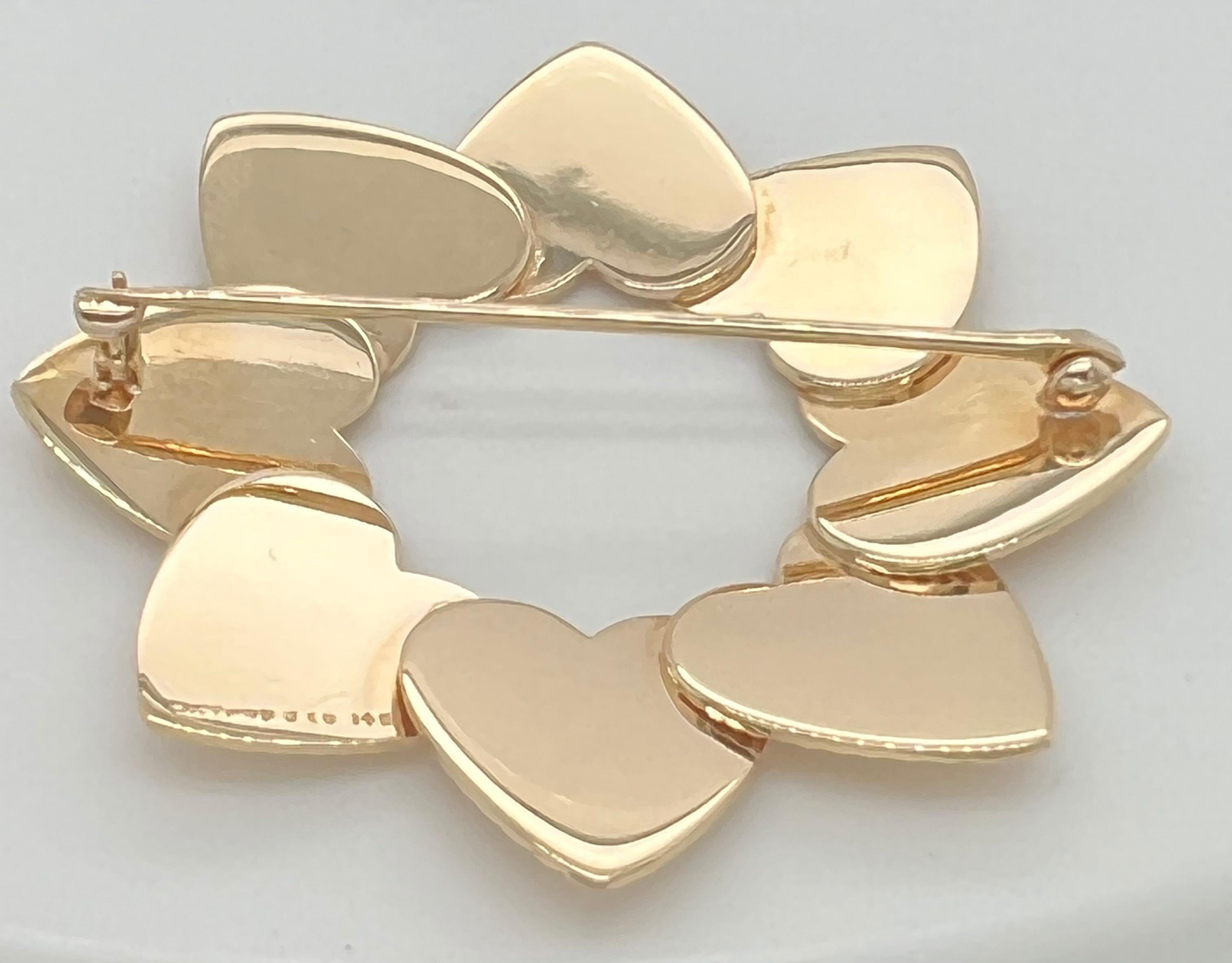 Chic retro heart pin.  Made and signed by TIFFANY & CO. Comprised of eight interlocking figural hearts, deeply engraved with a fine line pattern.  14K yellow gold.  1 3/4