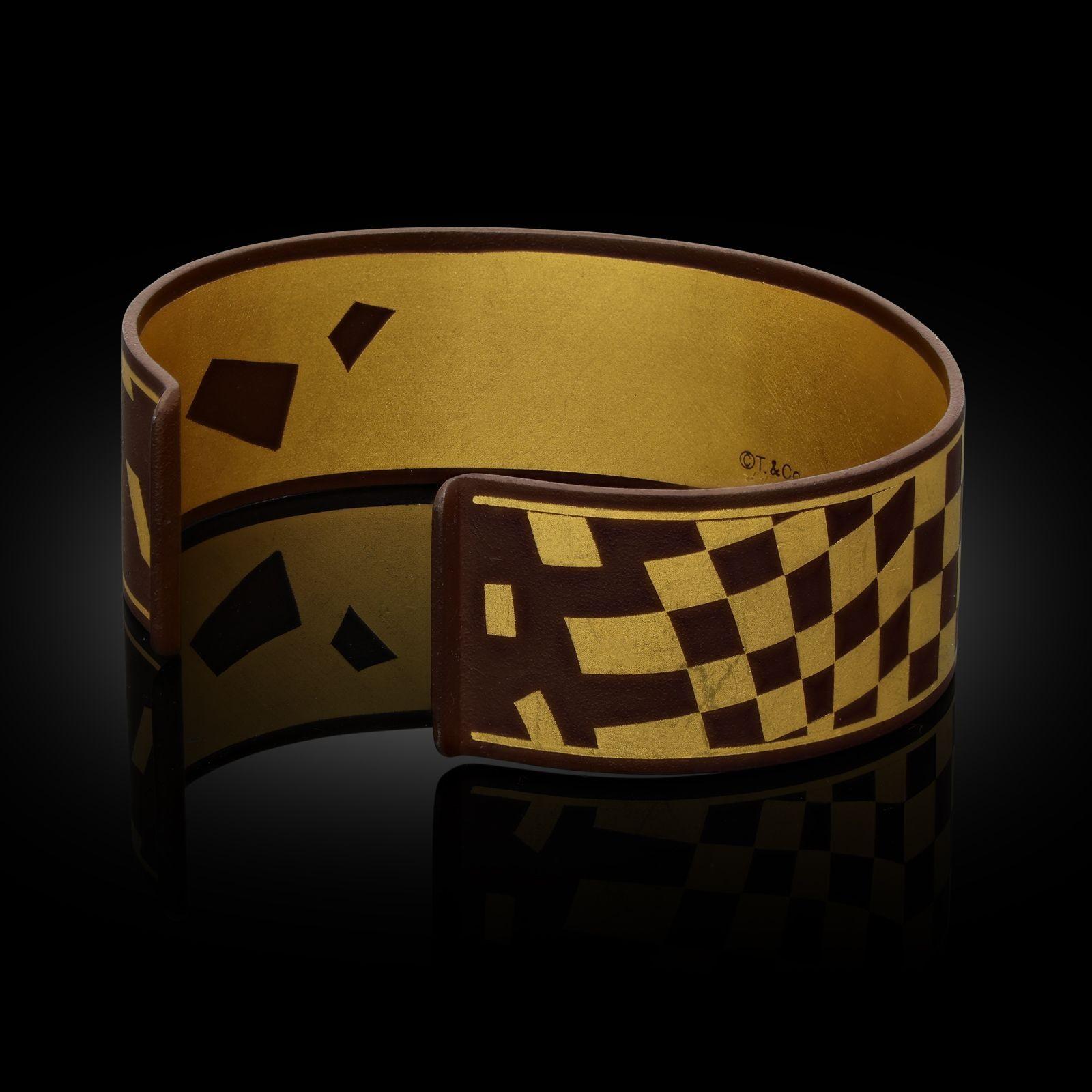 A striking gold, iron and lacquer 'Damascene' cuff bangle designed by Angela Cummings and made by Tiffany & Co. c.1979, the solid cuff measuring 2cm wide with an opening at the back, formed of iron which has been applied with a rich brown lacquer
