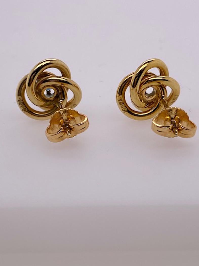 Classic knot earrings, set with a faceted sapphire in the center.  Made and signed by TIFFANY & CO.  !8K yellow gold.  1/2