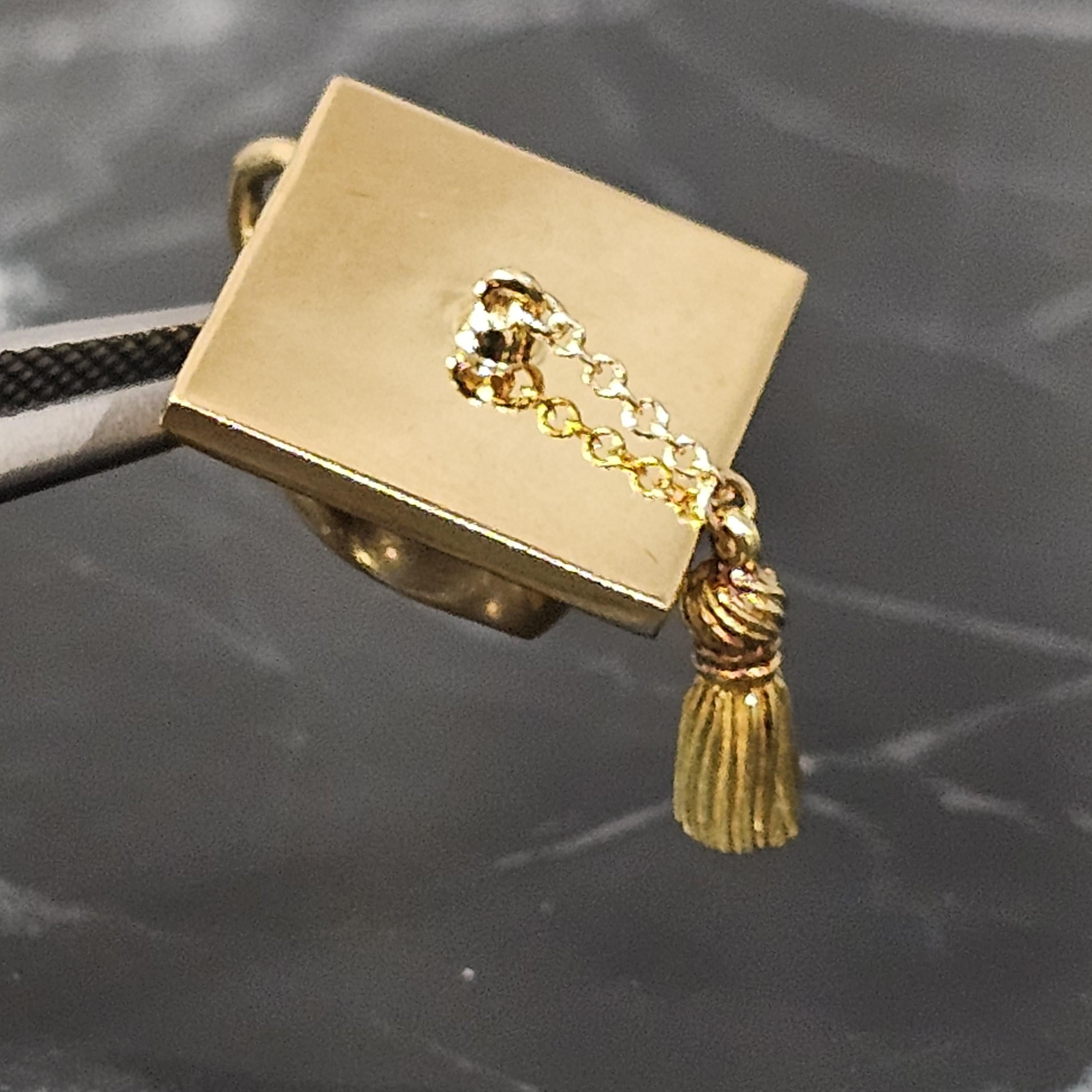 Questo raffinato ciondolo di Tiffany & Co. è un pezzo unico, realizzato in oro giallo 18 carati, con un dettagliato disegno di un cappello di laurea. Questo ciondolo è perfetto per chi apprezza i gioielli finemente lavorati con un tocco di