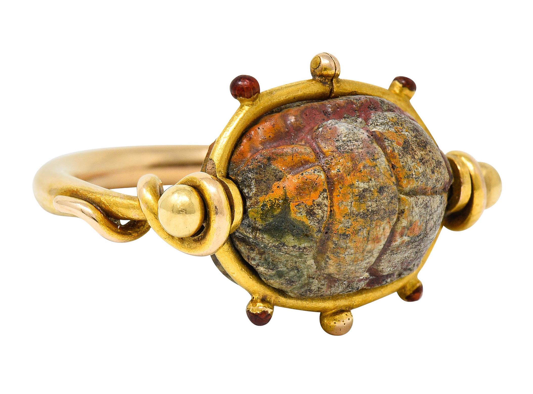 Handwrought ring centering an oval hardstone cabochon

Deeply carved to depict a scarab motif while underside depicts hieroglyphics

Opaque bluish green with remnants of yellow and red faience

With a gold surround accented by gold beading - with
