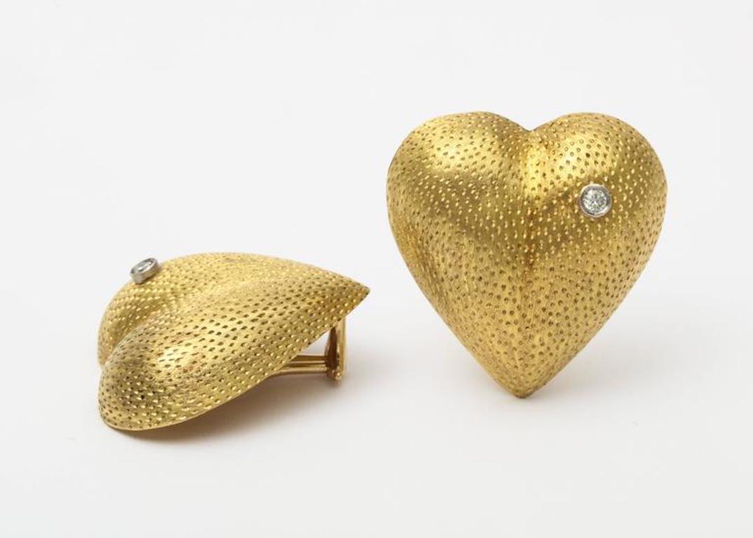 A charming pair of vintage Tiffany heart form clip earrings in stippled 18 k gold with a bezel set diamond. Unlike most US Tiffany these were made in Italy in 18 k gold. Also note the diamonds are artistically with asymmetric set diamonds