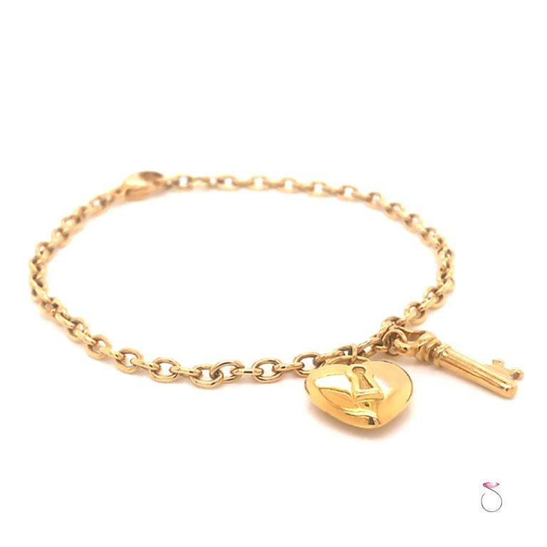 Authentic Tiffany & Co. heart and key charm bracelet in 18K yellow gold. This bracelet features oval cable links with two charms. The heart charm has a high polish finish and measures 14.35 mm x 12.50 mm x 4.72 mm. The key charm has a high polish