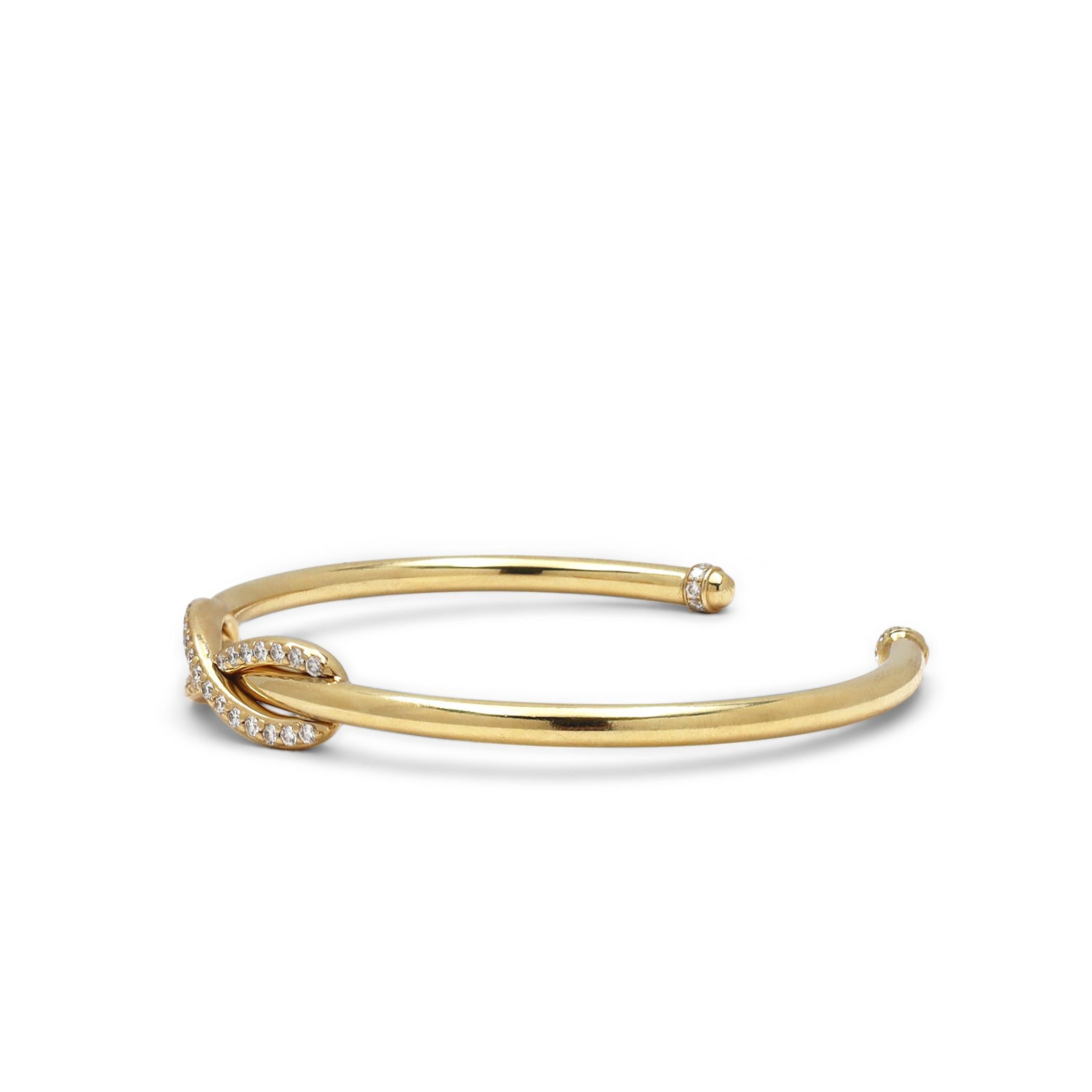 Authentic Tiffany & Co. 'Infinity' cuff bracelet crafted in 18 karat yellow gold.  A single infinity motif set with an estimated .30 carats of round brilliant cut diamonds encircles the bracelet at its center.  Each domed end is set with an