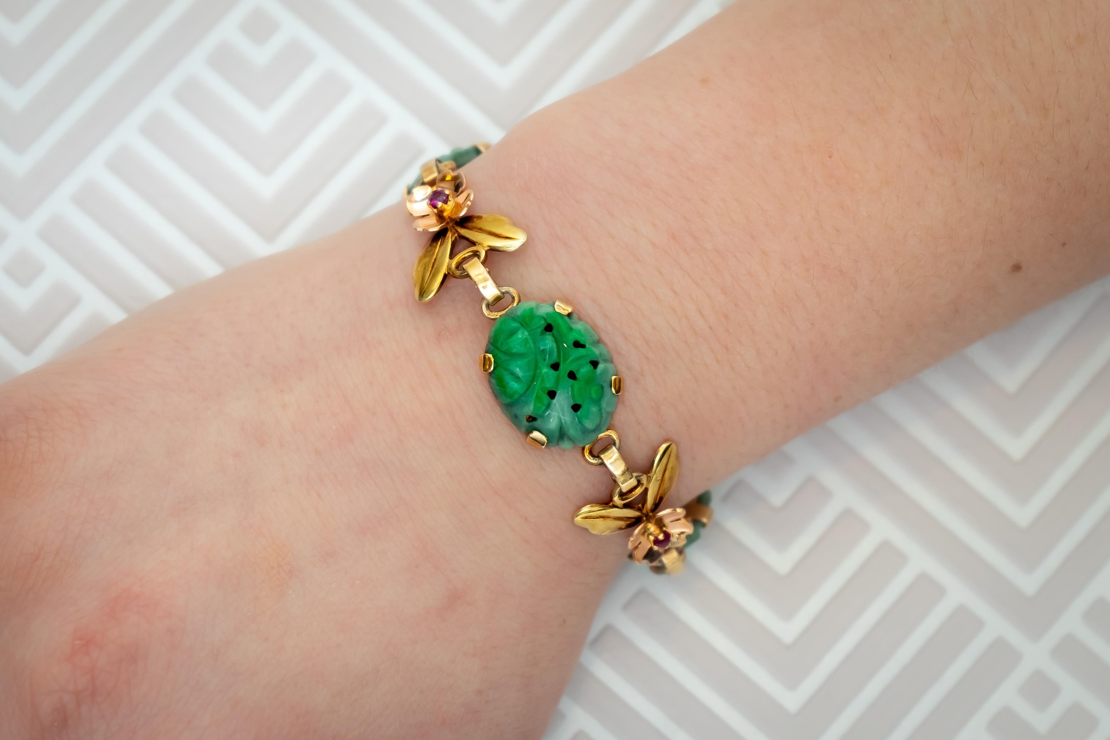 A vintage Tiffany & Co jade bracelet, the gold links comprising four quatrefoil rose gold flowers each with a central claw set ruby and two yellow gold leaves, alternating with three carved oval jadeite panels, signed Tiffany & Co, 14k, length