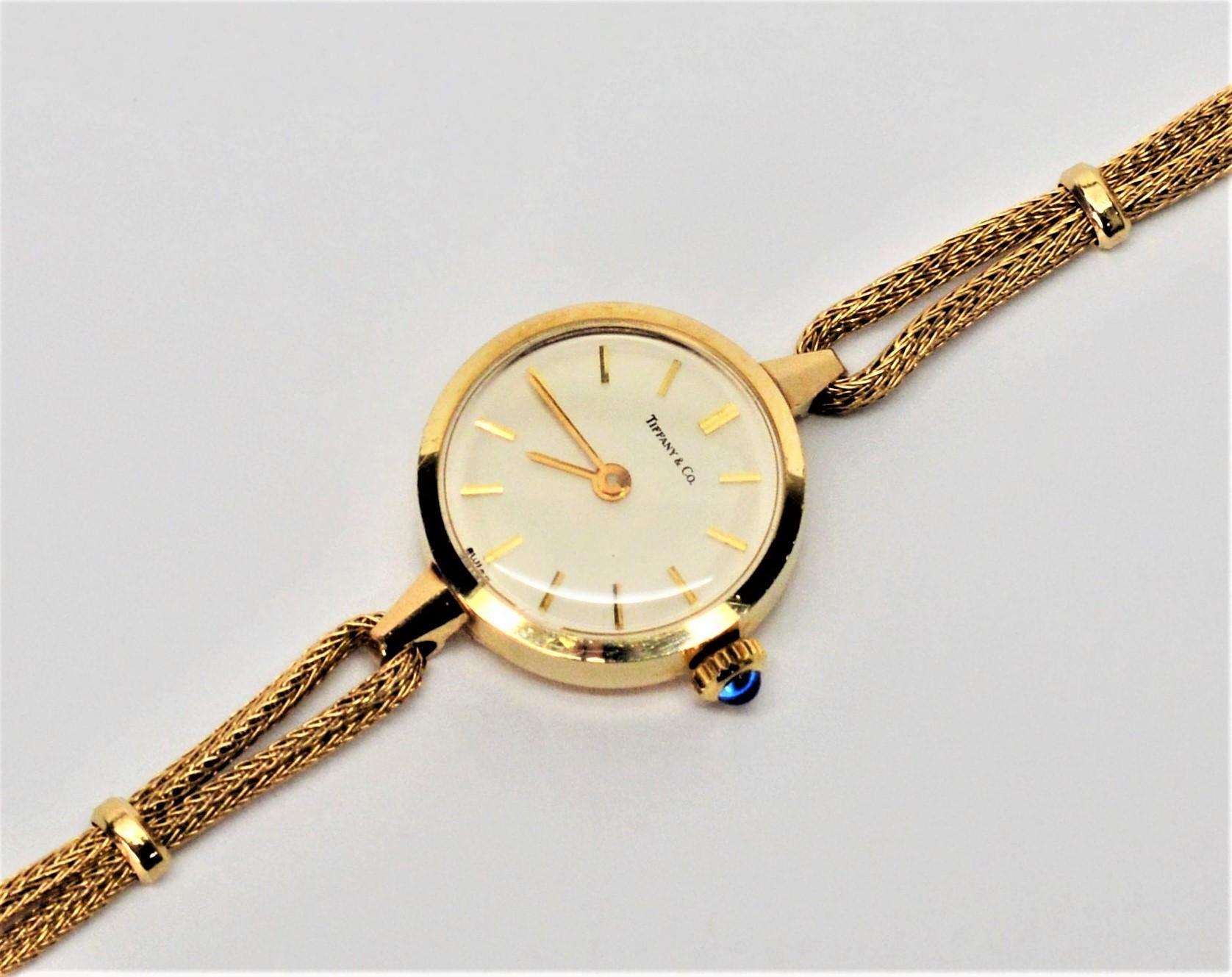 Elegant simplicity describes this Tiffany & Co. Ladies 14K fourteen karat yellow gold dress wrist watch. Measures 3/4 inch round with a white face, signed by Tiffany & Co. and gold stick markers. The case back has an engraved personalized message