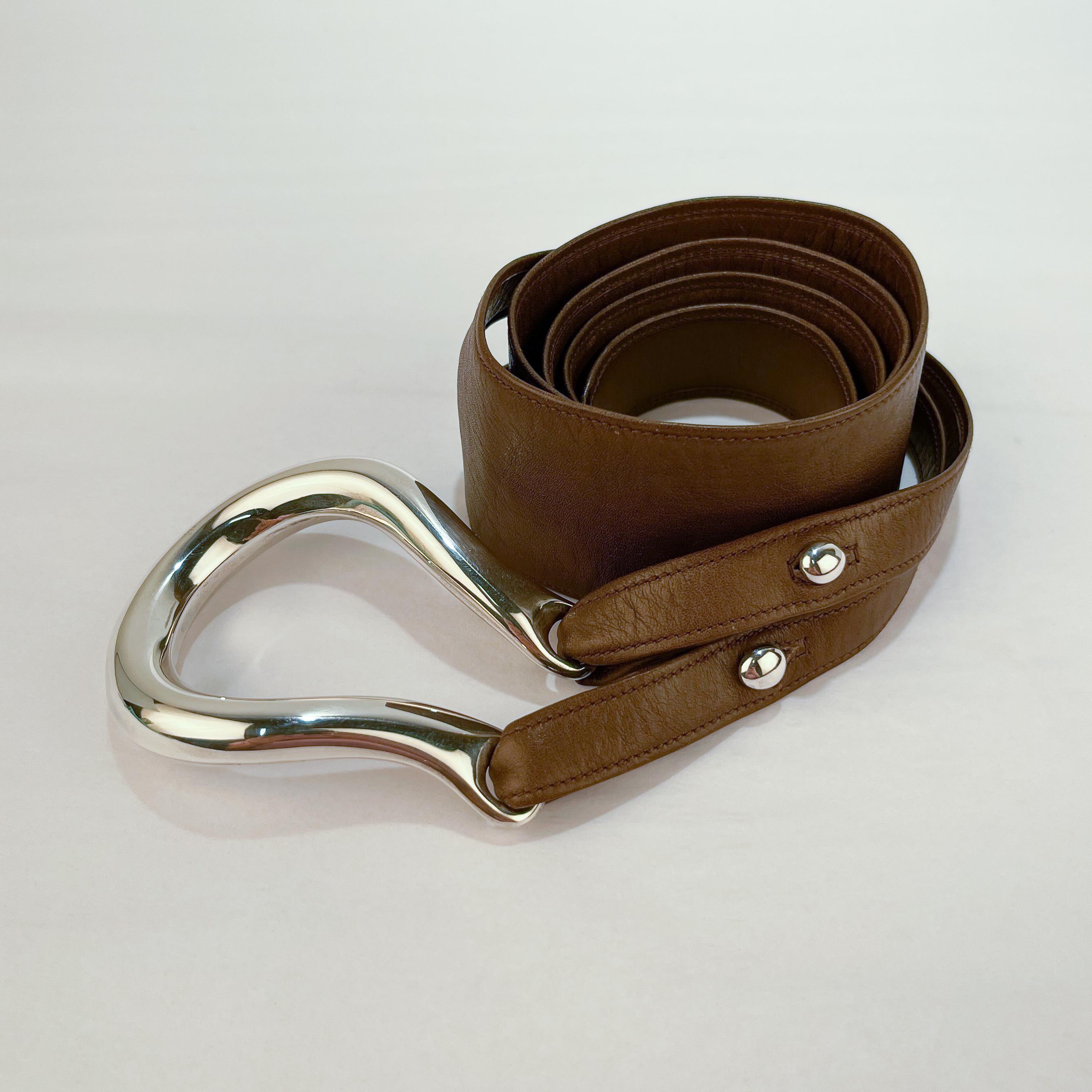 A fine Tiffany & Co. leather belt.

Consisting of a split strap brown leather belt and sterling silver horseshoe shaped buckle and buttons. The leather belt loops through the buckle for closure and variable sizings.

Designed by Elsa Peretti in the