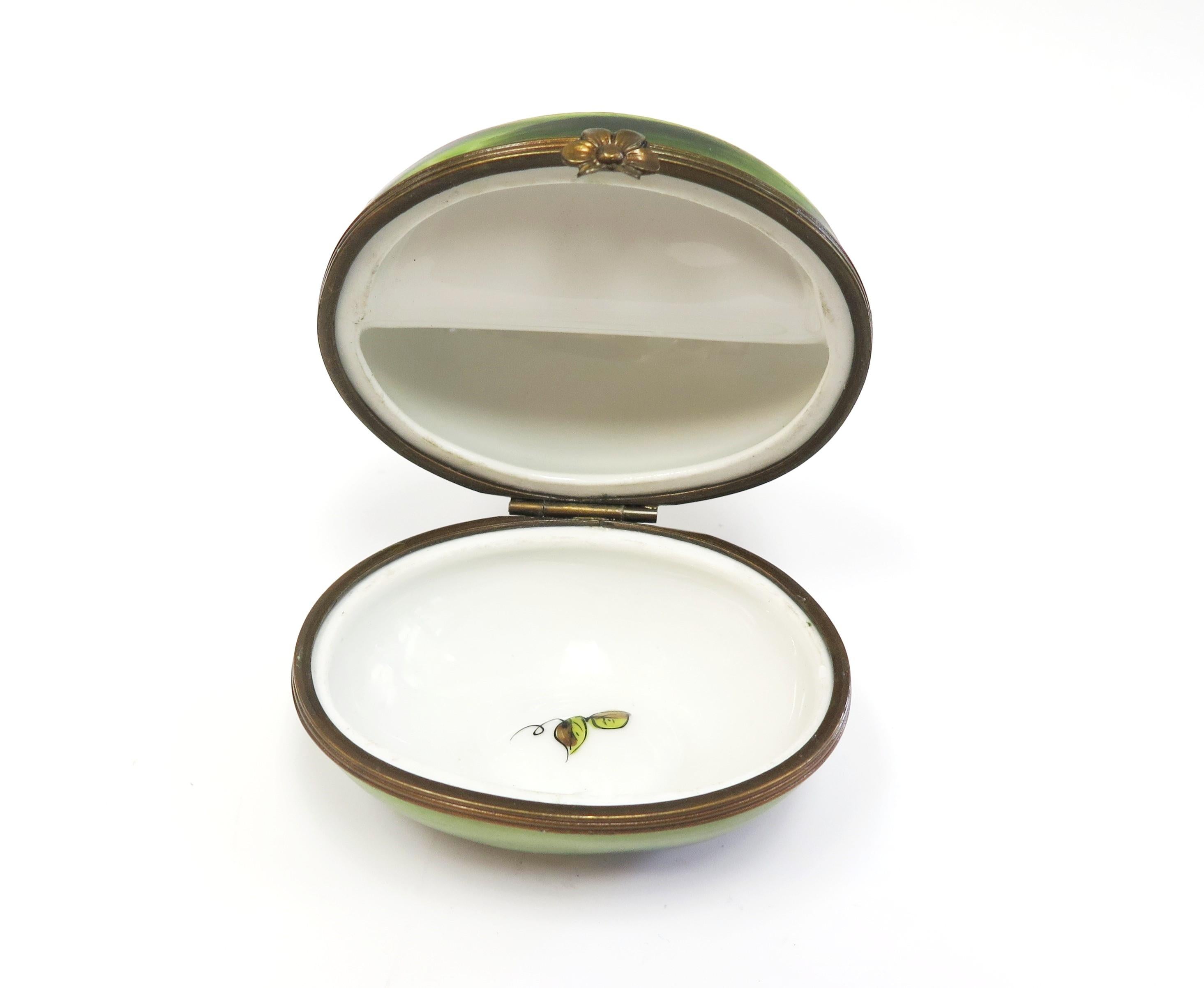Tiffany & co hand painted Limoges box in the form of a watermelon with a quarter cut off and showing the red interior with the black seeds. The watermelon box opens in the middle with a hinged lid and is white on the inside. The exterior is dark