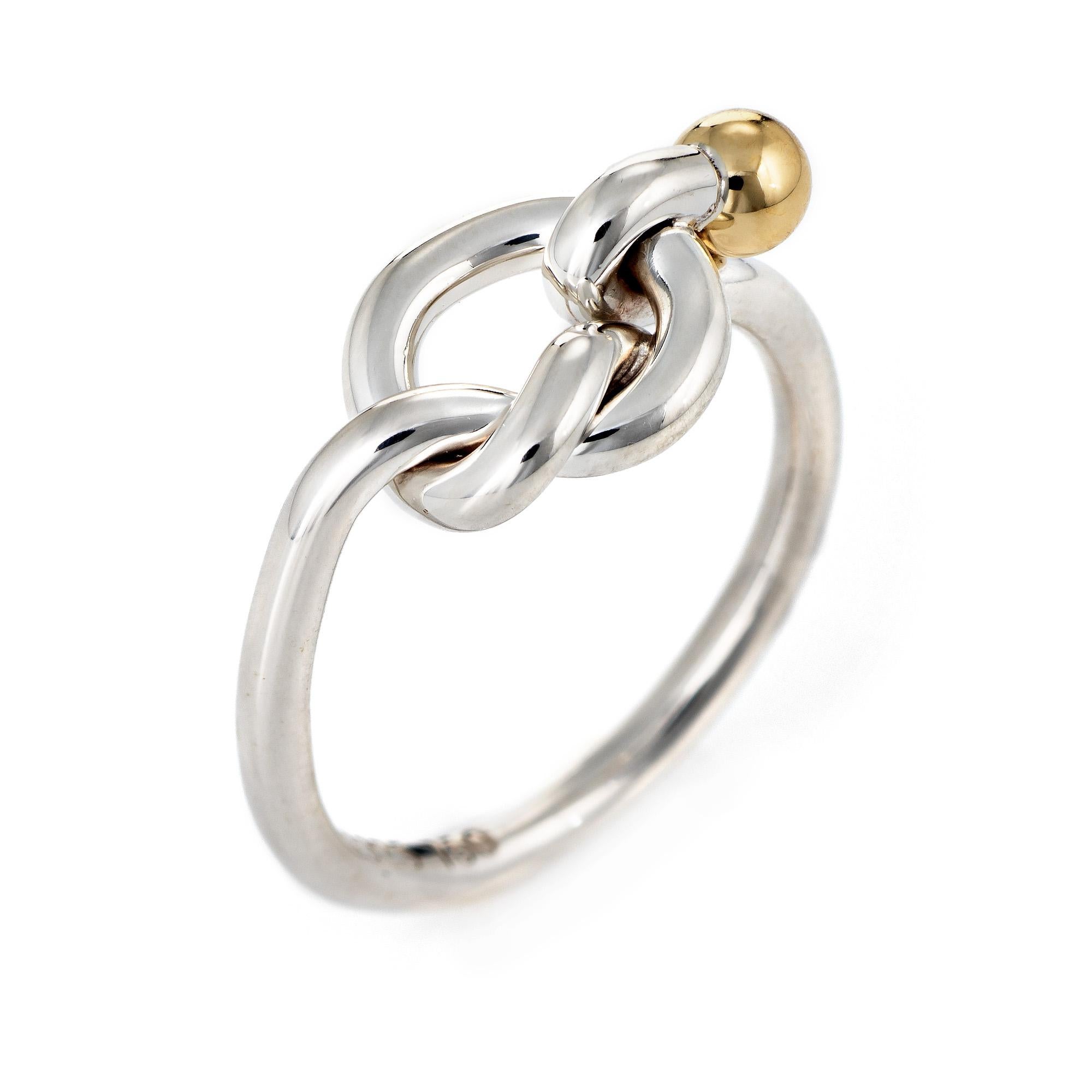 Finely detailed pre-owned Tiffany & Co love knot ring crafted in sterling silver & 18 karat yellow gold. 

The stylish ring features a love knot finished with an 18k yellow gold orb. The low rise ring (3.5mm - 0.13 inches) sits comfortably on the