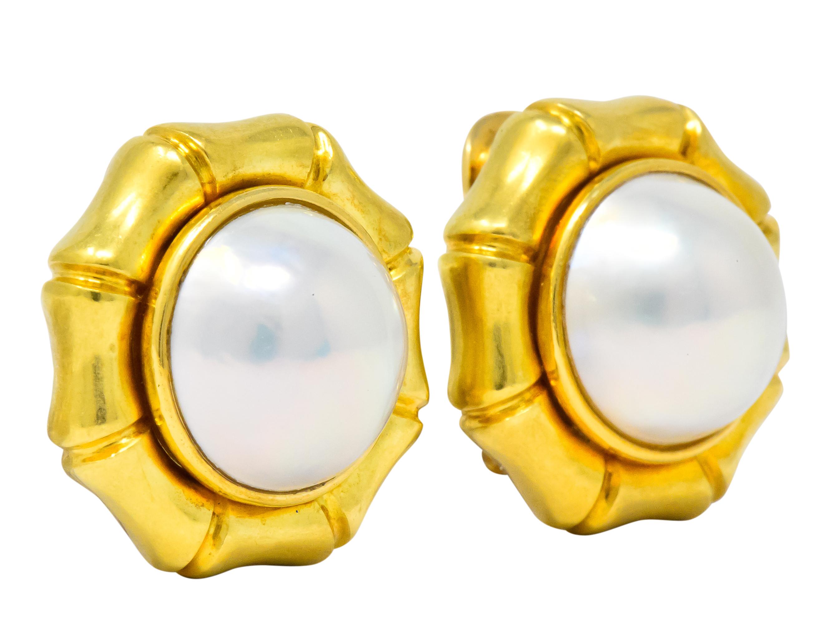 Each centering a mabe pearl measuring approximately 15.0 mm, gray body color with strong spectral overtone and very good luster

Bezel set in matte gold surround featuring a bamboo motif

Hinged omega clip-backs with optional articulated
