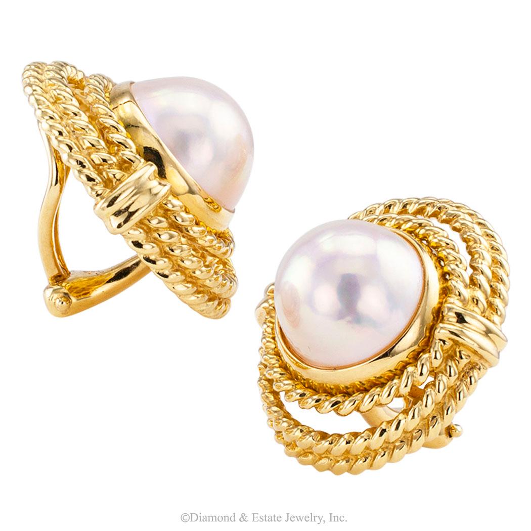 Tiffany & Co mabe pearl and gold clip on earrings circa 1990. Featuring a pair of mabe pearls measuring approximately 12 mm, bezel-set in an oval-shaped stepped border of cable gold, omega clip backs, mounted in 18-karat yellow gold, signed Tiffany