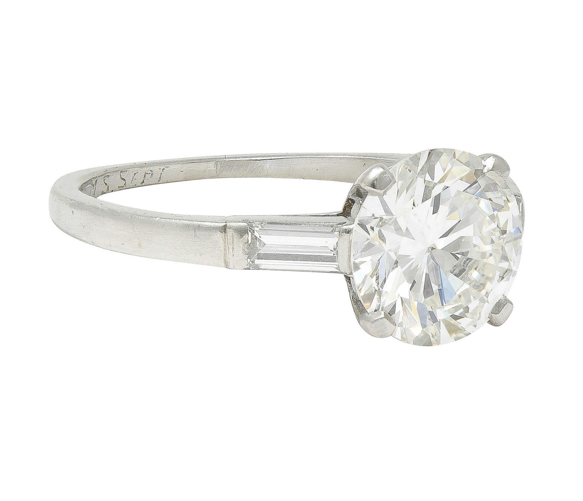 Centering a round brilliant cut diamond weighing 1.82 carats - H color with VVS2 clarity
Prong set in basket - flanked by baguette cut diamonds bar set in cathedral shoulders
Weighing approximately 0.18 carat total - eye clean and bright
Shank is