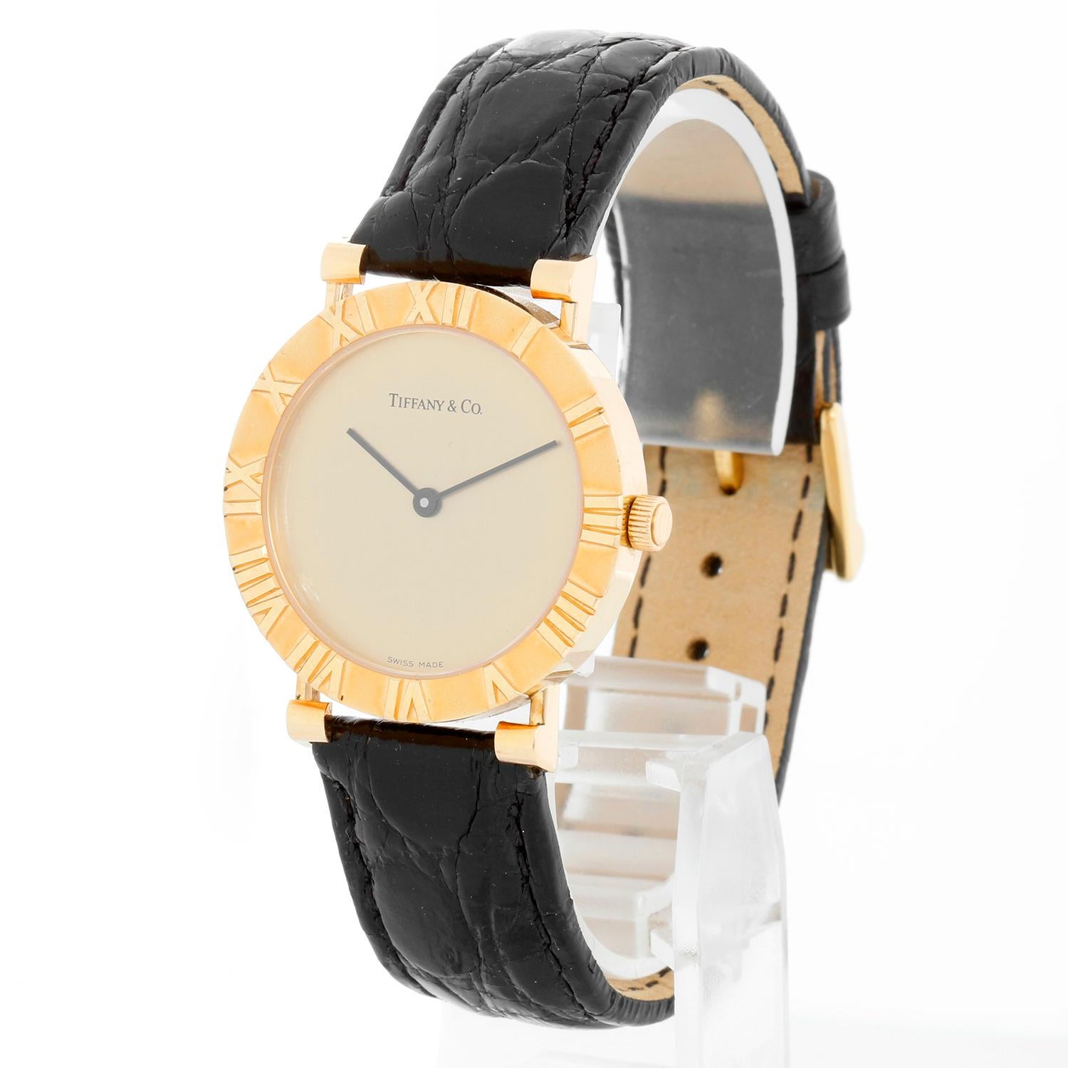 Tiffany & Co. Midsize Atlas 18K Yellow Gold Watch Ref. 0630 - Quartz. 18K Yellow gold round style case with raised roman numerals on bezel (31 mm) . Champagne dial signed Tiffany & Co.. Black alligator pattern strap with Tiffany & Co. yellow gold