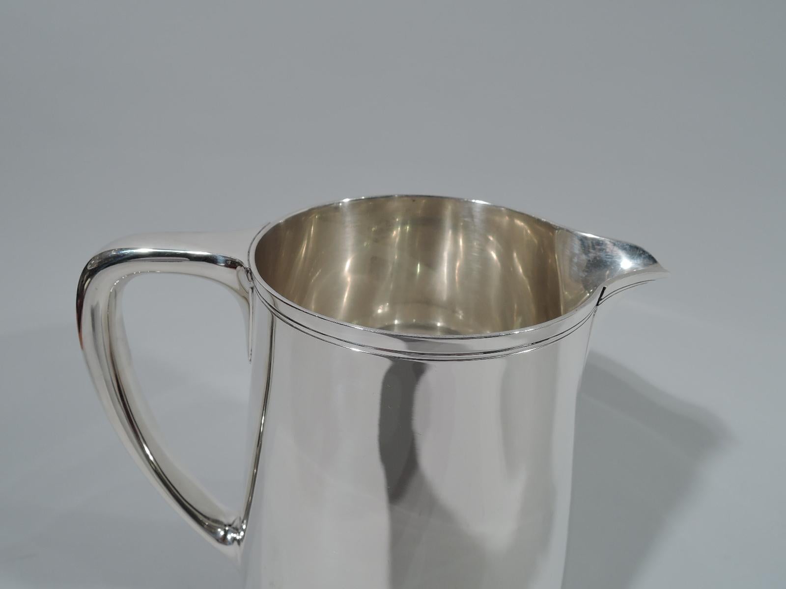Sterling silver water pitcher. Made by Tiffany & Co. in New York. Upward tapering sides, scrolled bracket handle, and V-spout. Softened Modernism with spare incised banding wrapping around rim and spout. Hallmark includes pattern no. 22343 (first