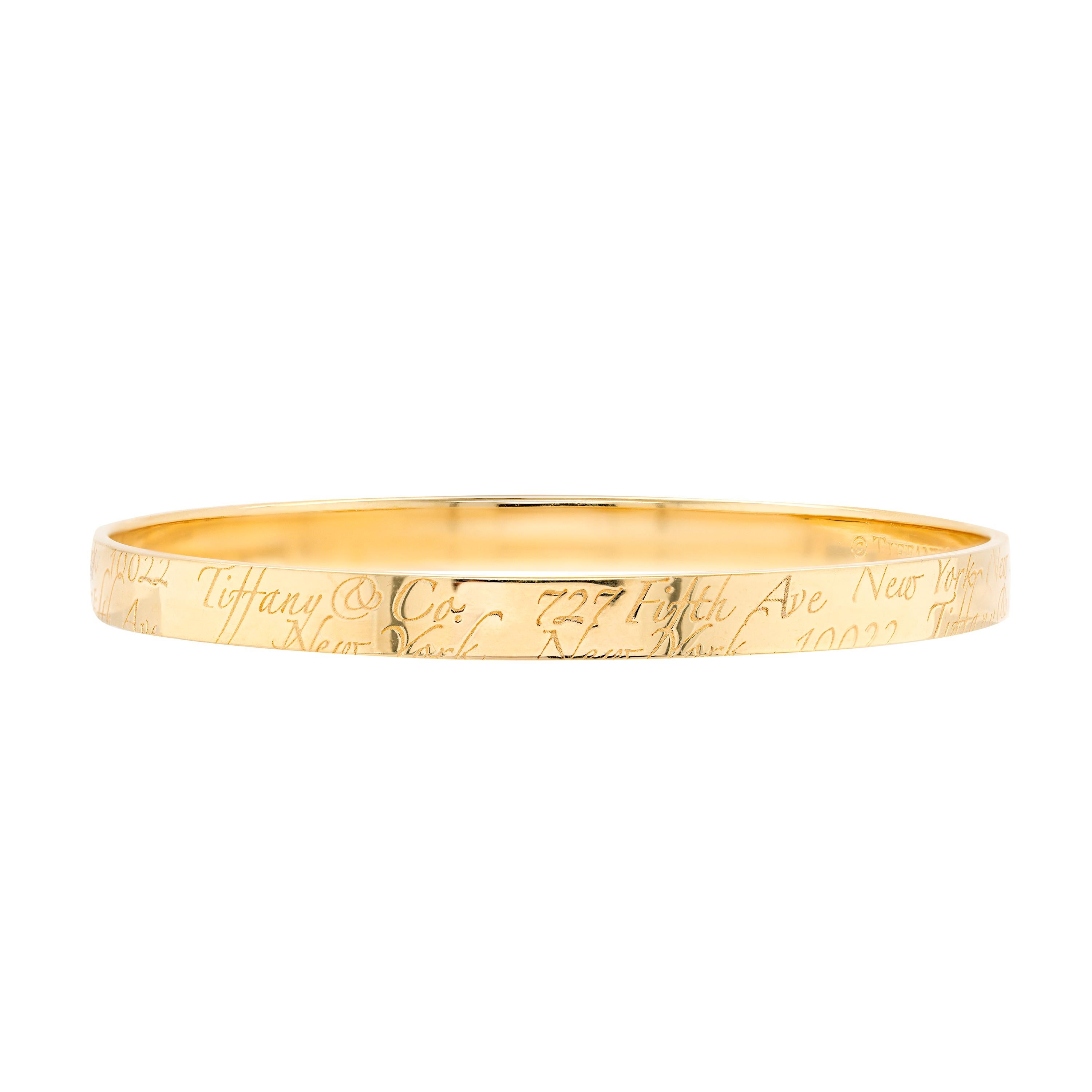 Tiffany & Co solid gold bangle engraved Tiffany & Co 727 Fifth Avenue New York 10022 in script throughout. The bangle weighs a total of 26 grams, measures 5.8mm in width and has an approximate circumference of 7.5 inches. Stamped TIFFANY & CO. 750.