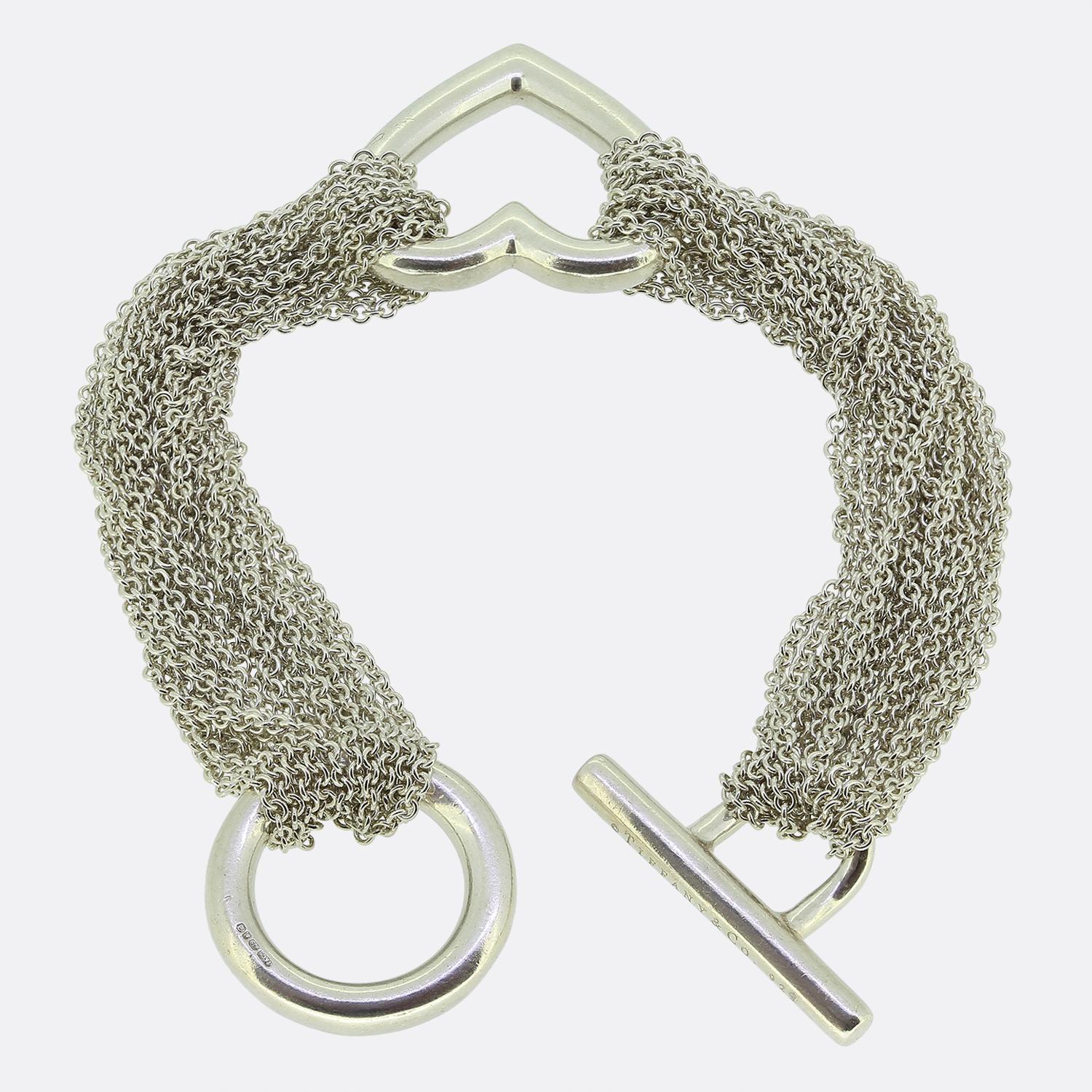 Aquí tenemos una emblemática pulsera de eslabones de la mundialmente conocida diseñadora de joyas Tiffany & Co. Esta pieza presenta un diseño de cadena belcher de varias vueltas interconectadas por un motivo abierto en forma de corazón en el centro.