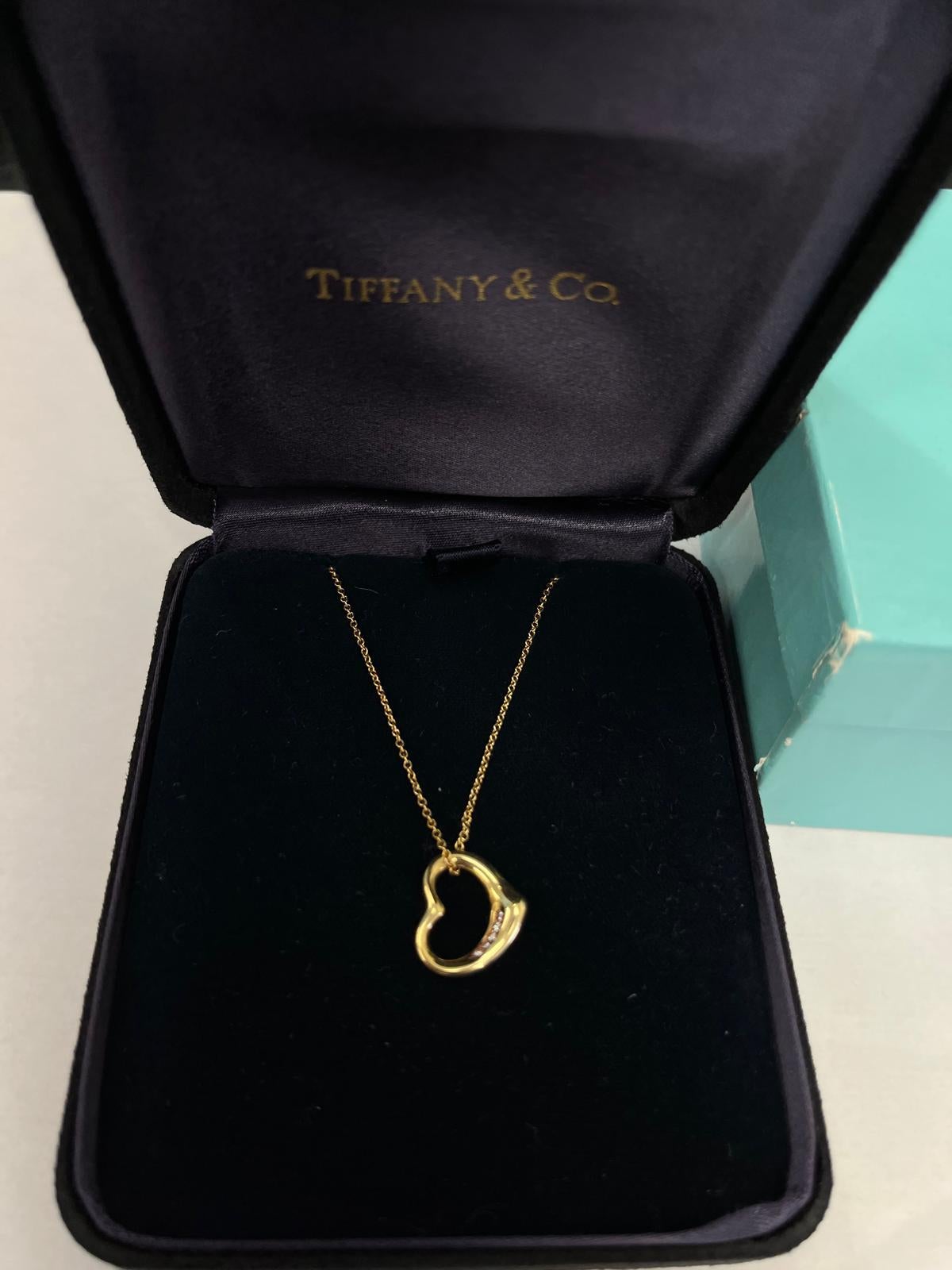 Este collar Corazón Abierto, una pieza elegante e icónica de Tiffany & Co., está elaborado en lujoso oro amarillo de 18 ct, engastado con 5 brillantes diamantes naturales a lo largo de la curva del corazón. Diseñado por Elsa Peretti, el corazón