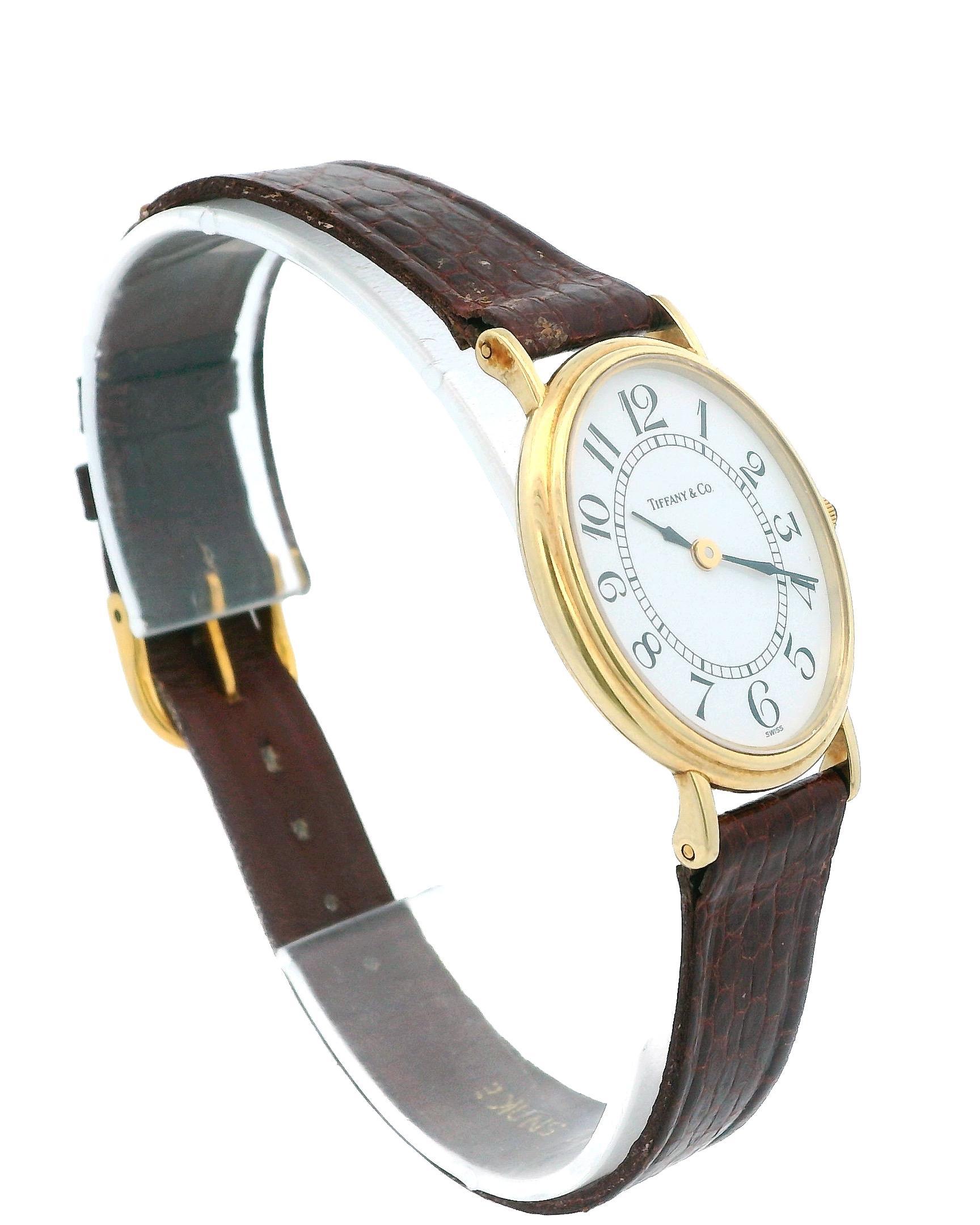 Eine elegante Uhr von Tiffany & Co. mit einer raffinierten ovalen Form, die von einem präzisen Quarzwerk angetrieben wird. Das weiße 24-mm-Zifferblatt ist mit klassischen arabischen Ziffern verziert, die von einer glatten 14-karätigen Goldlünette