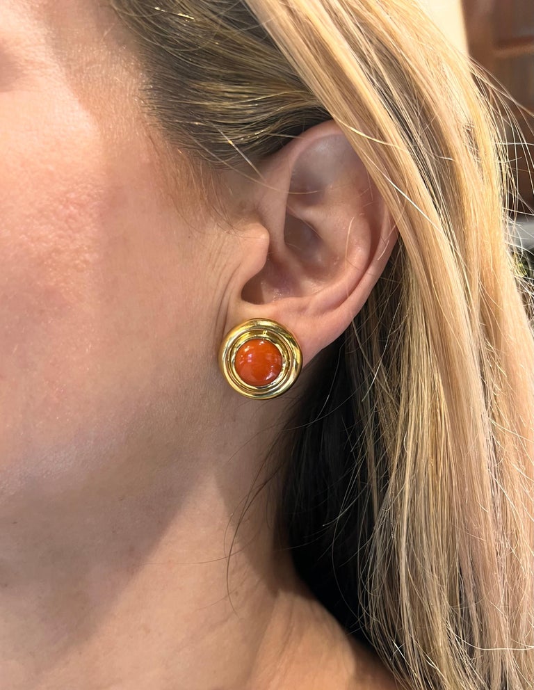 Created by iconic designer Paloma Picasso for Tiffany & Co, these 18k yellow gold circular clip earrings have a polished double bezel design each inset with a salmon-orange color, natural coral cabochon measuring approximately 11.50mm in diameter. 