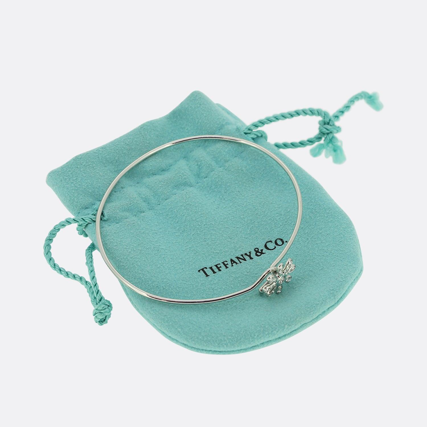 This is a platinum bangle from the luxury jewellery designer Tiffany & Co. Paloma Picasso iconic daisy design offers flexibility and stylish simplicity. The bangle features a central daisy design setting set with brilliant cut diamonds and crafted