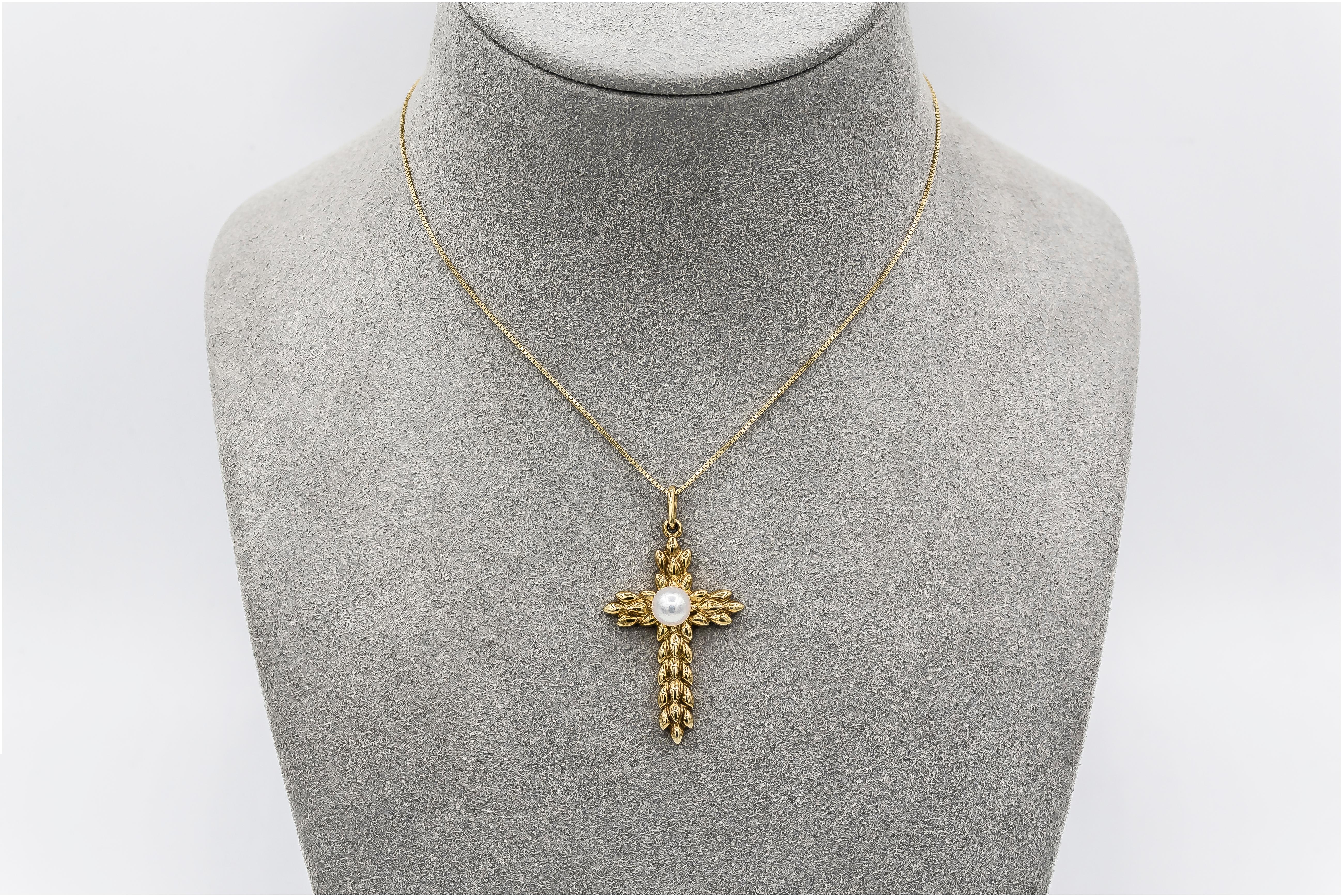 18 karat yellow gold pendant necklace showcasing a cross made with gold leaves, set with a pearl center.  Attached to an 18 inch yellow gold chain. Made and signed by Tiffany & Co. 