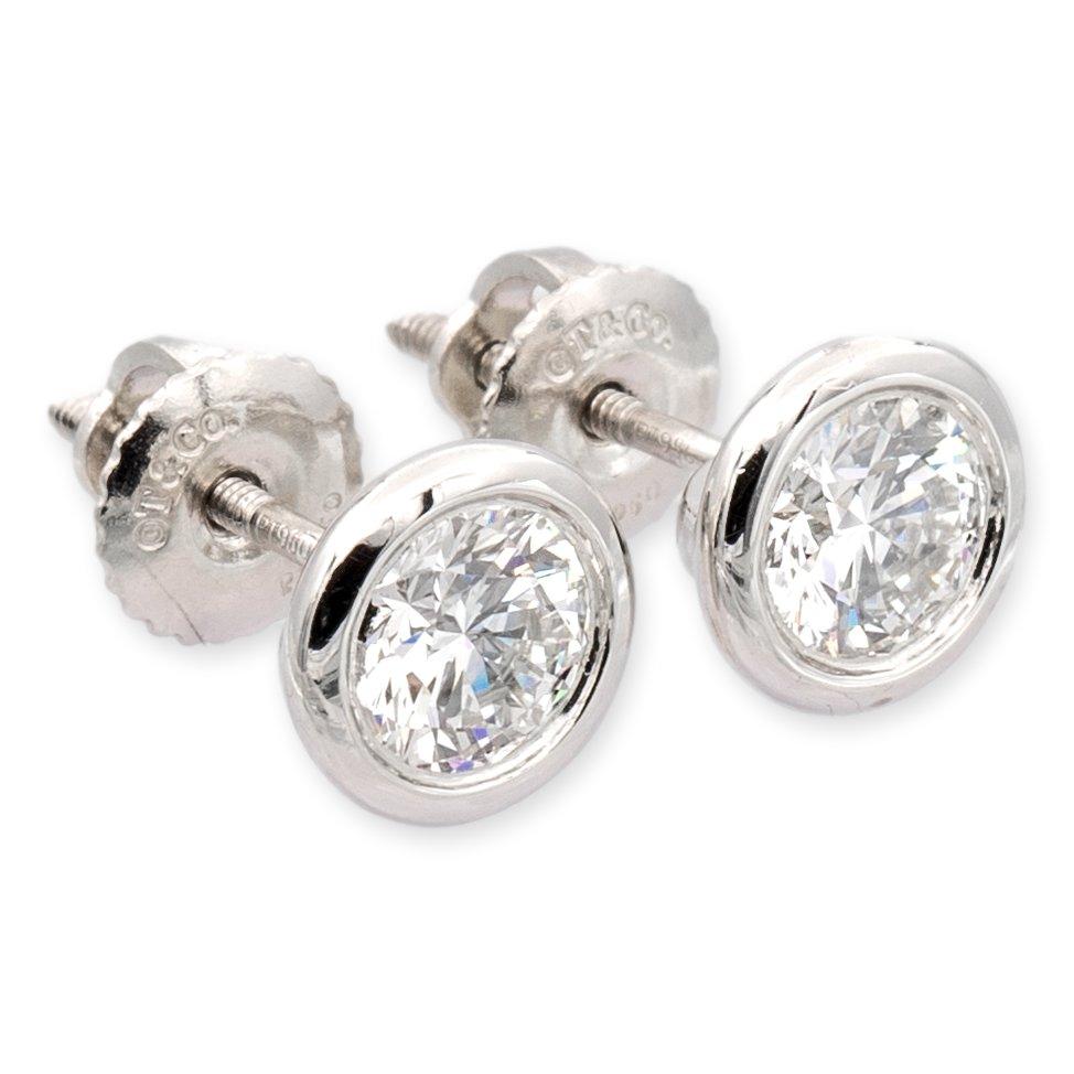 Tiffany and Co. diamond by the yard stud earrings designed by Elsa Peretti finely crafted in platinum featuring 2 round brilliant cut bezel-set diamonds weighing 0.60 cts each for a total of 1.20 cts. F-G color and VS clarity. Screw-back posts 
and