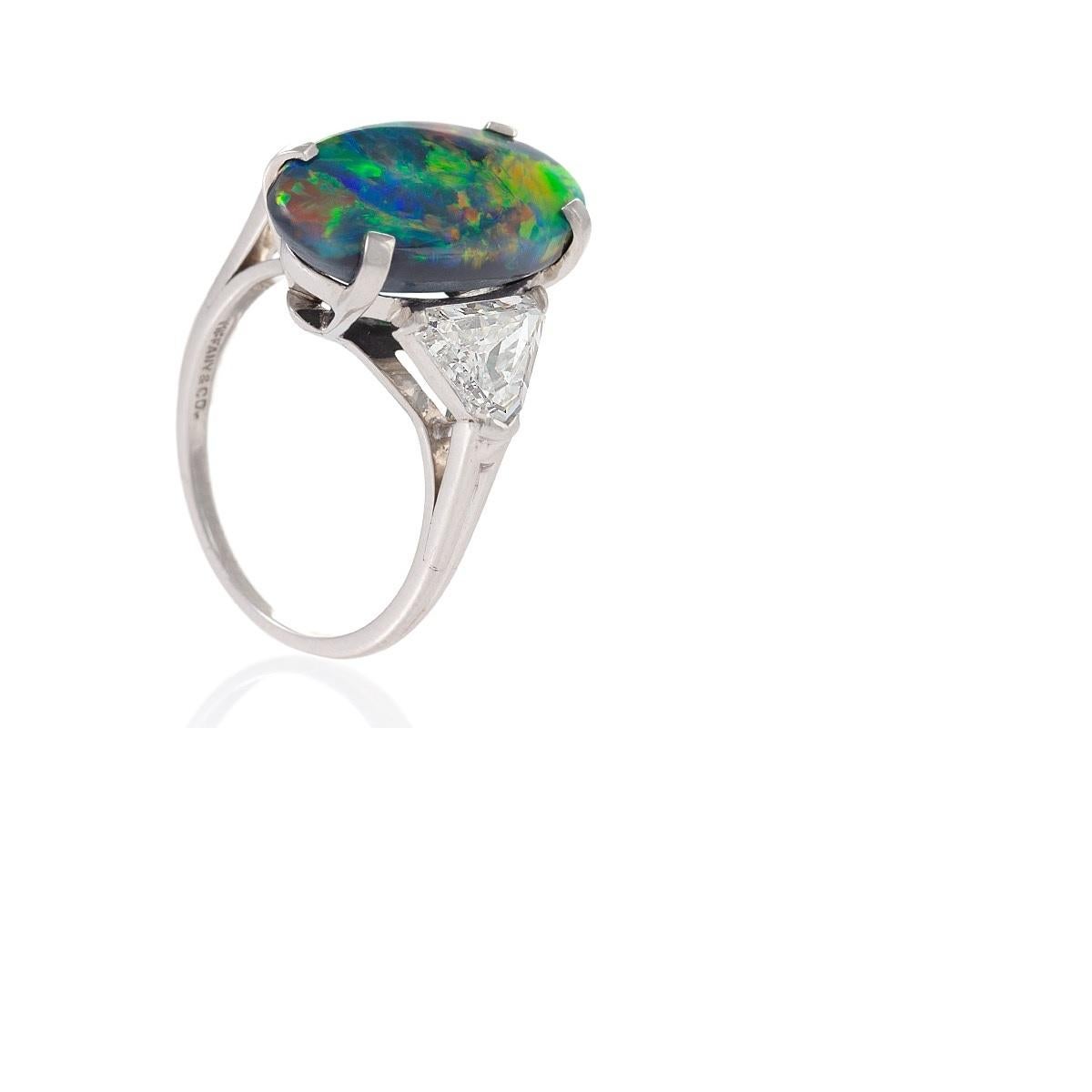 An American modern platinum ring with black opal and diamonds by Tiffany & Co. The ring is set with a cabochon black opal with an approximate total weight of 5.00 carats, flanked by shield-shaped diamonds with an approximate total weight of 1.40