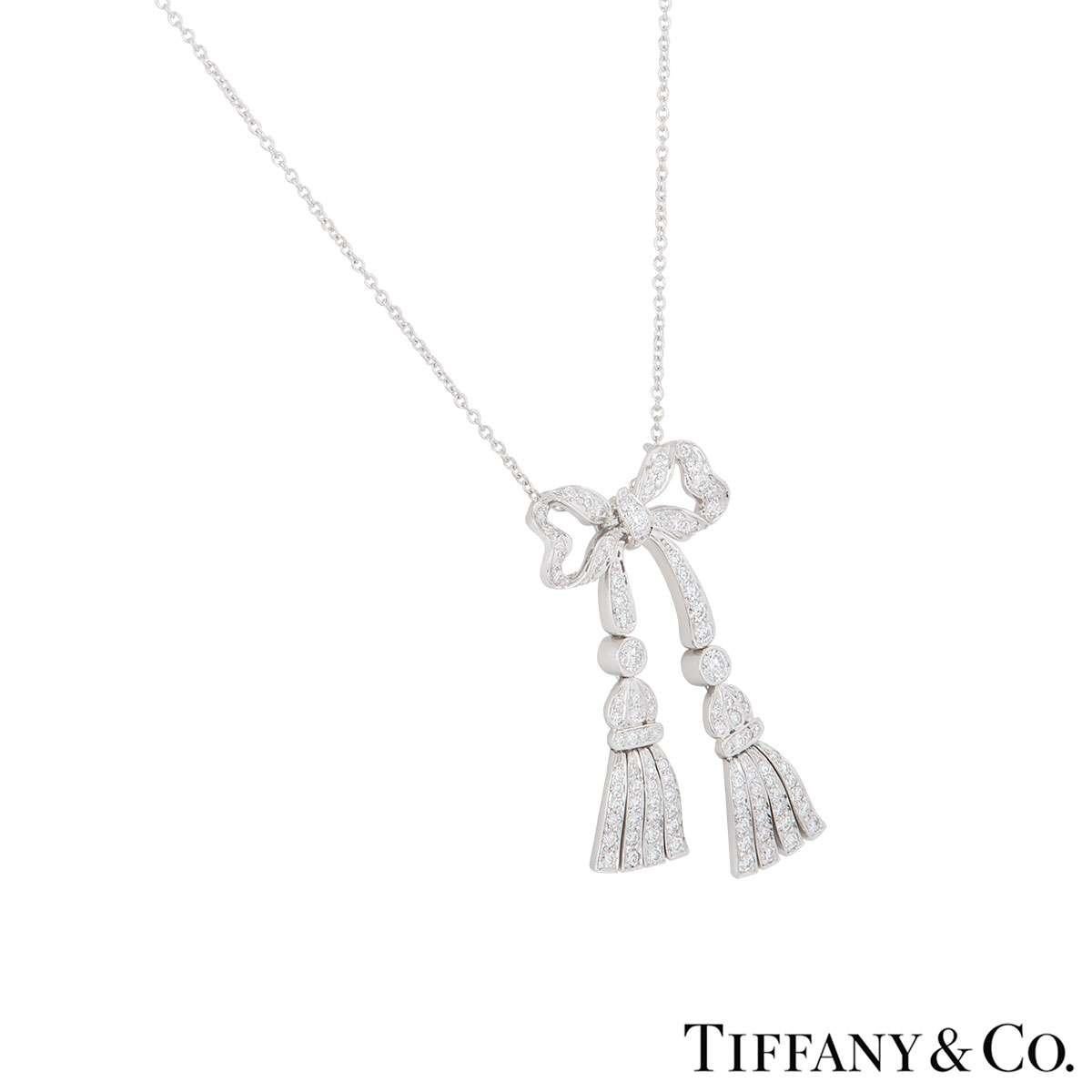 A striking diamond bow necklace in platinum by Tiffany & Co. The central bow motif suspends two articulated tassel pendants, each connected to a single rubover set diamond. The bow is pave set with round brilliant cut diamonds totaling approximately