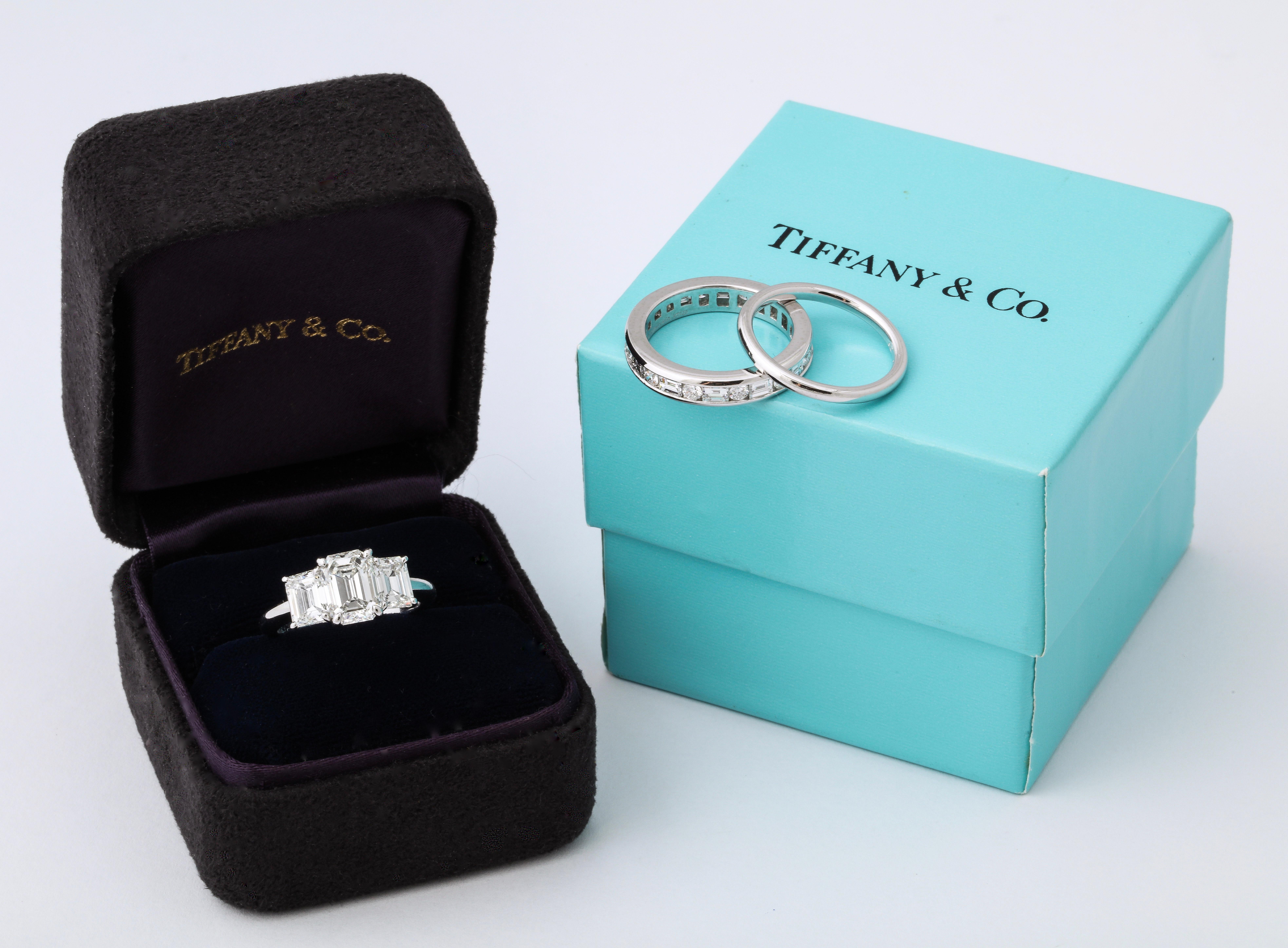 This completely intact set consisting of an emerald cut three stone diamond engagement ring, a diamond eternity band and a platinum wedding band is an extremely rare find in today's market.  The set even comes complete with the original Tiffany &