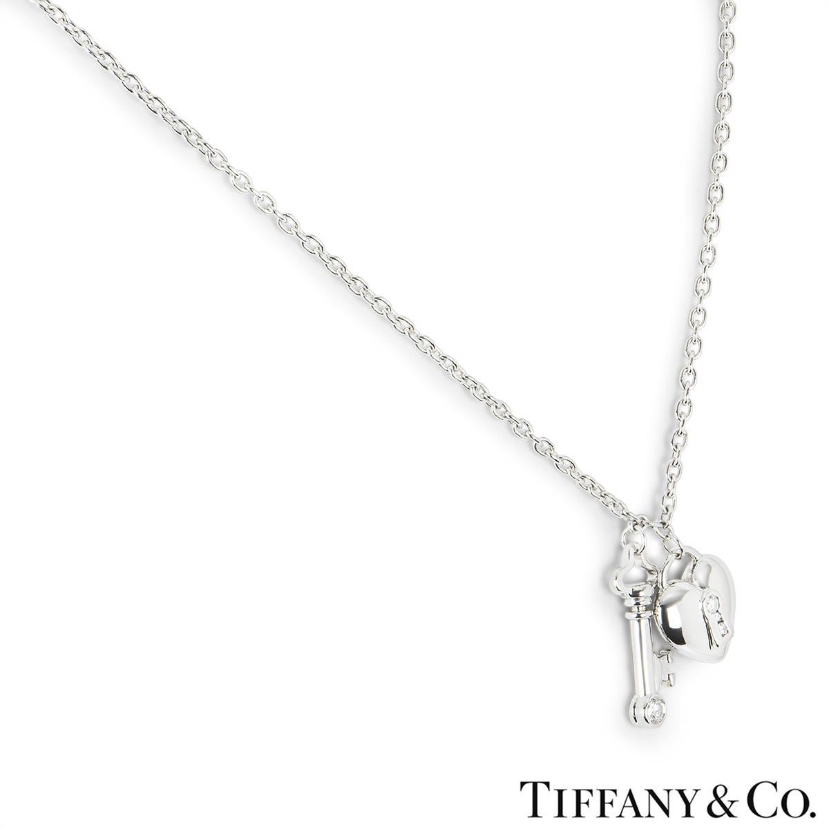 A platinum diamond key and lock pendant by Tiffany & Co. The pendant features a key charm set with a single round brilliant cut diamond and a heart shaped lock set with 3 diamonds. The key measures 2.1cm in length and the heart measures 1.4cm in