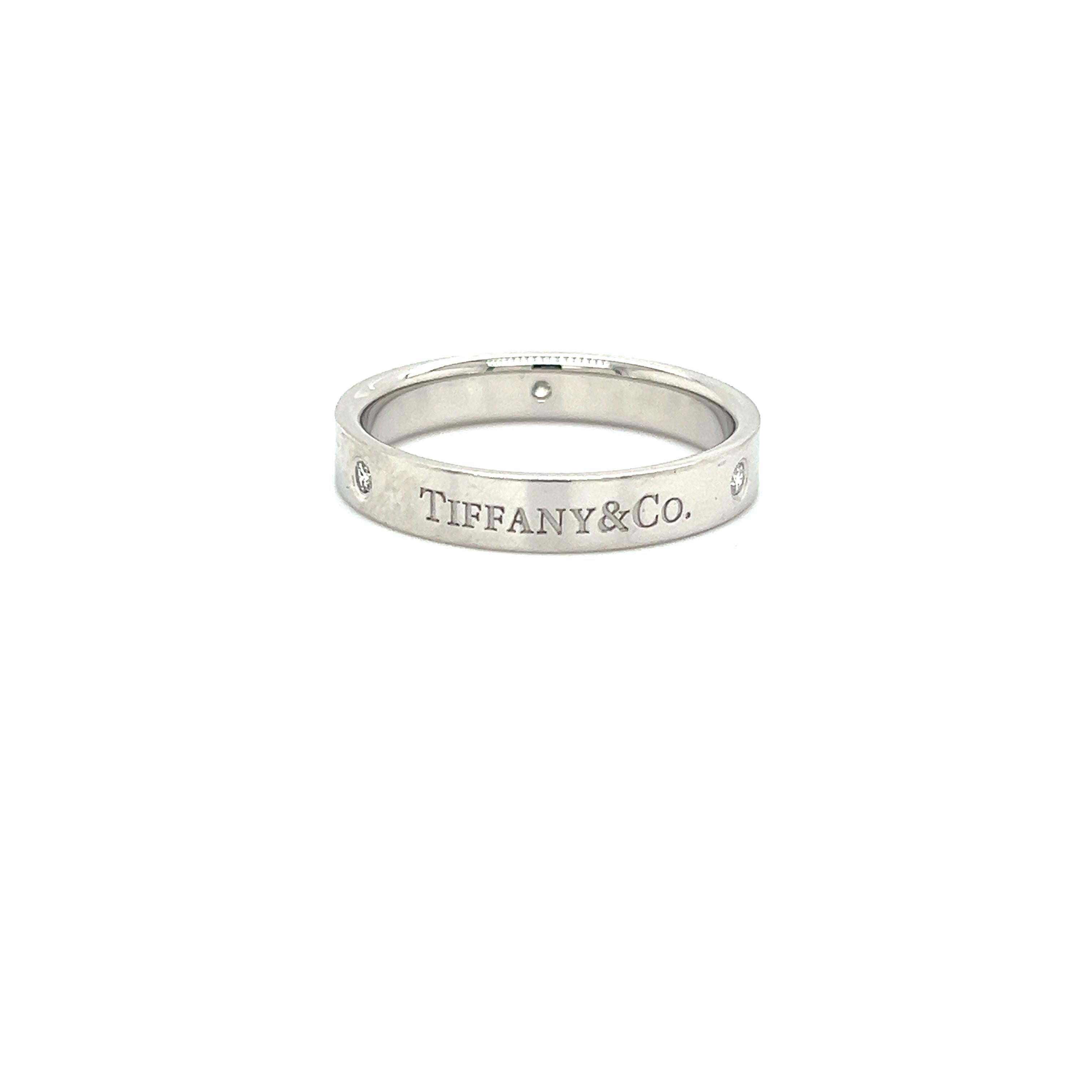 Classic design from famed designer Tiffany & Co. This ring is crafted in platinum and shows a 4 mm width. Three round brilliant cut diamonds are set into the design alternating with the brands logo 