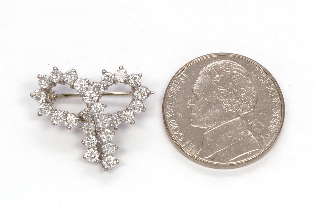 We are pleased to offer this Tiffany & Co. Platinum & Diamond Ribbon Pin Brooch. This finely crafted piece features an estimated 1.80ctw D-F/VVS-VS round brilliant cut diamonds set in a platinum ribbon motif. It measures 0.75 x 0.75 inches in size.