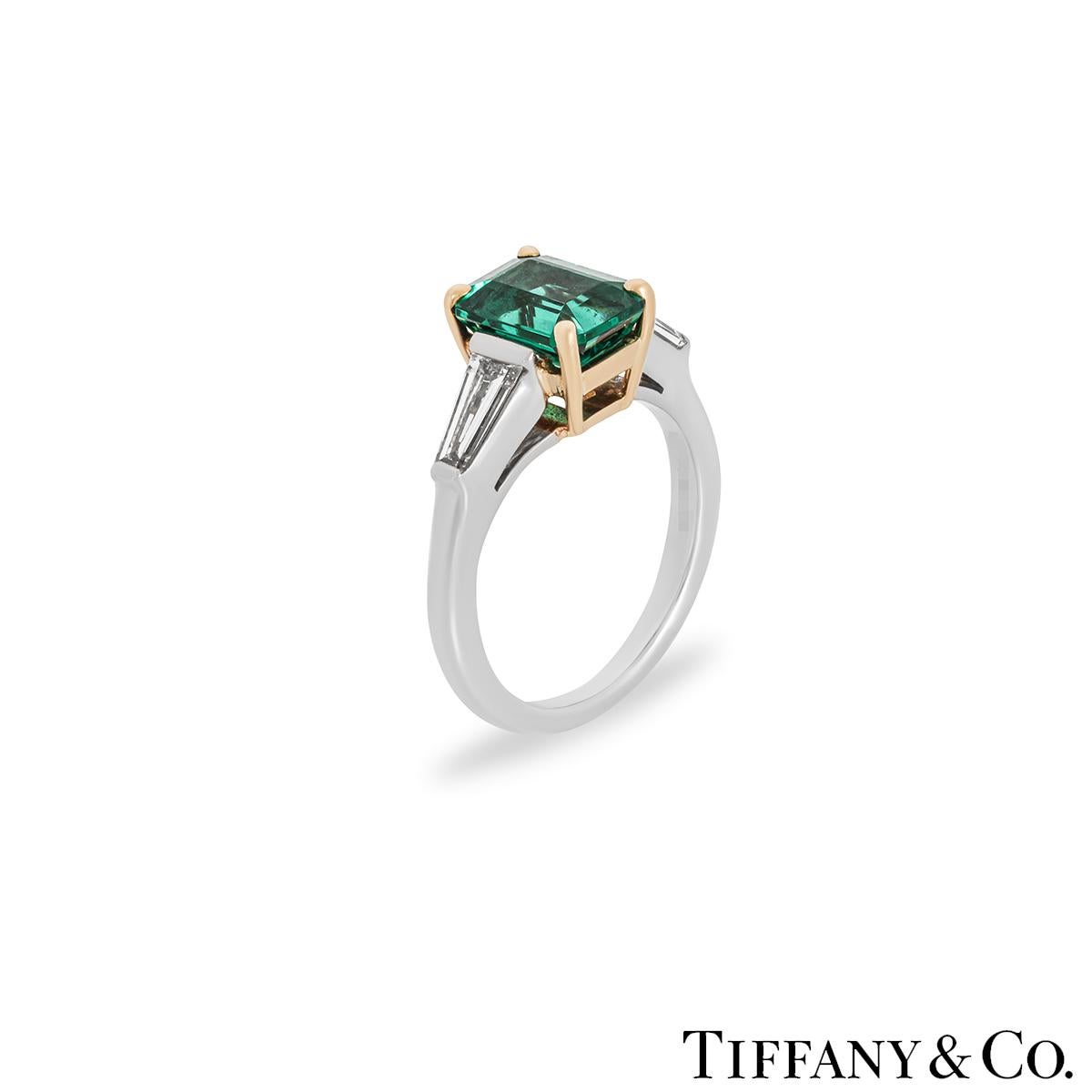 An exceptional platinum and 18k yellow gold emerald and diamond ring from Tiffany & Co. Adorning the centre of this three stone ring is an emerald cut emerald set in a yellow gold four prong mount, weighing 1.61ct and displaying a vivid green hue.