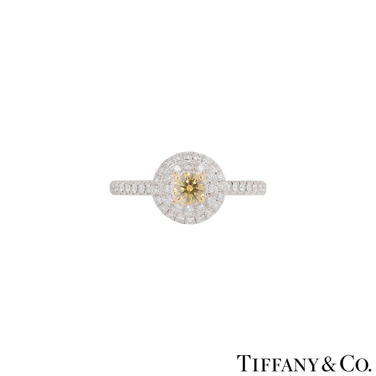 An alluring platinum diamond ring by Tiffany & Co. from the Soleste collection. The ring comprises of a fancy yellow round brilliant cut diamond in the centre surrounded by double pave set diamonds in a halo setting and on the shoulders. The fancy