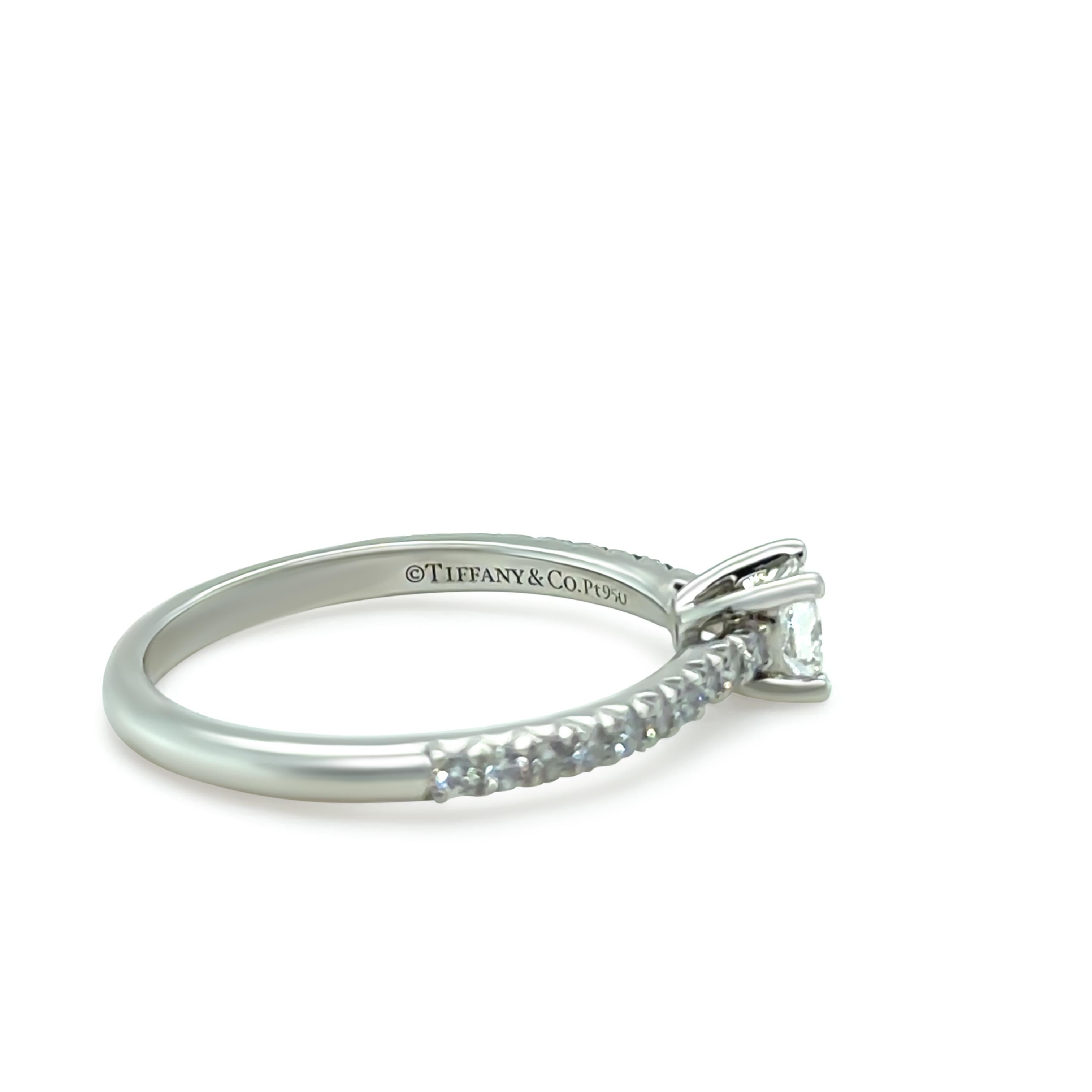 Diese exquisite Tiffany & Co. Der Verlobungsring Novo ist aus Platin gefertigt und mit einem modifizierten Diamanten im Prinzess-Schliff von 0,23 Karat besetzt, der für seine außergewöhnliche Brillanz bekannt ist.

Der Diamant in der Mitte ist in