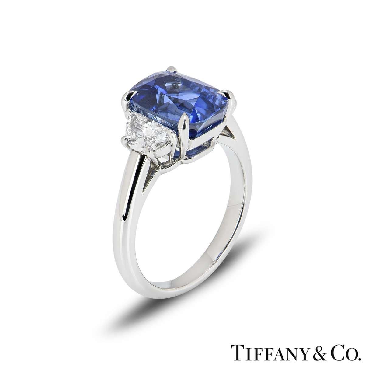 An exquisite sapphire and diamond ring by Tiffany & co. The ring is set to the centre with a cushion cut blue sapphire weighing 4.50ct, displaying a bright even hue. The sapphire is flanked by two half-moon cut diamonds totalling 0.58ct, E colour