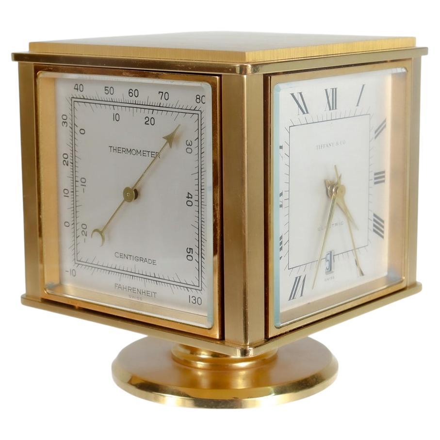 A fine midcentury weather station clock. 

By Tiffany & Co.

Meant for the desktop.

In two-tone high polished and brushed brass.

With a rotating cube top 4 function weather station supported by a brass pedastal base.

Functions include a
