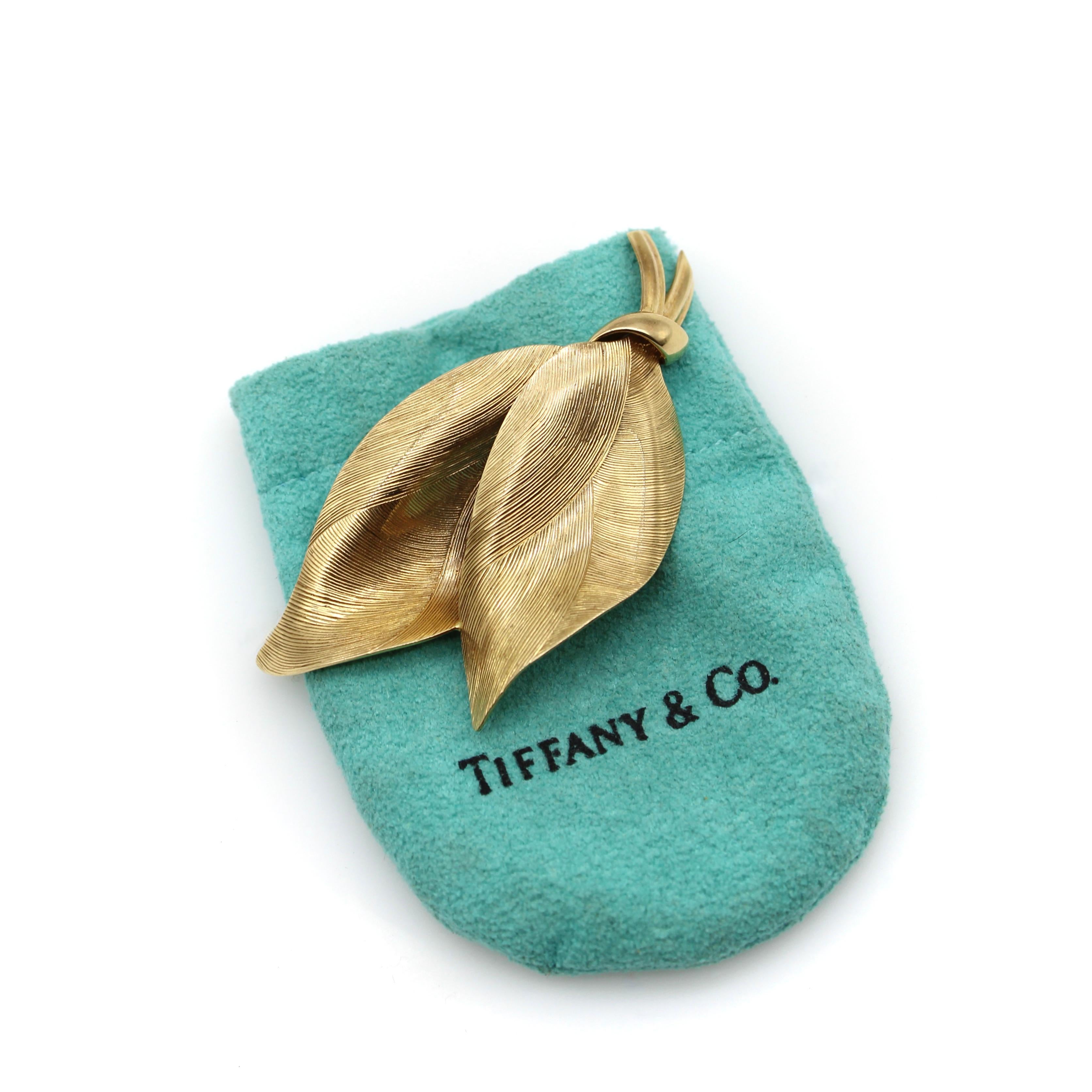 A classic Tiffany & Co. design, this 14k gold brooch is an abstract version of leaves with swaths of texture. The gold is hand-engraved with swooping lines that catch the light from many angles. The dual leaves nestle into each other and are tied