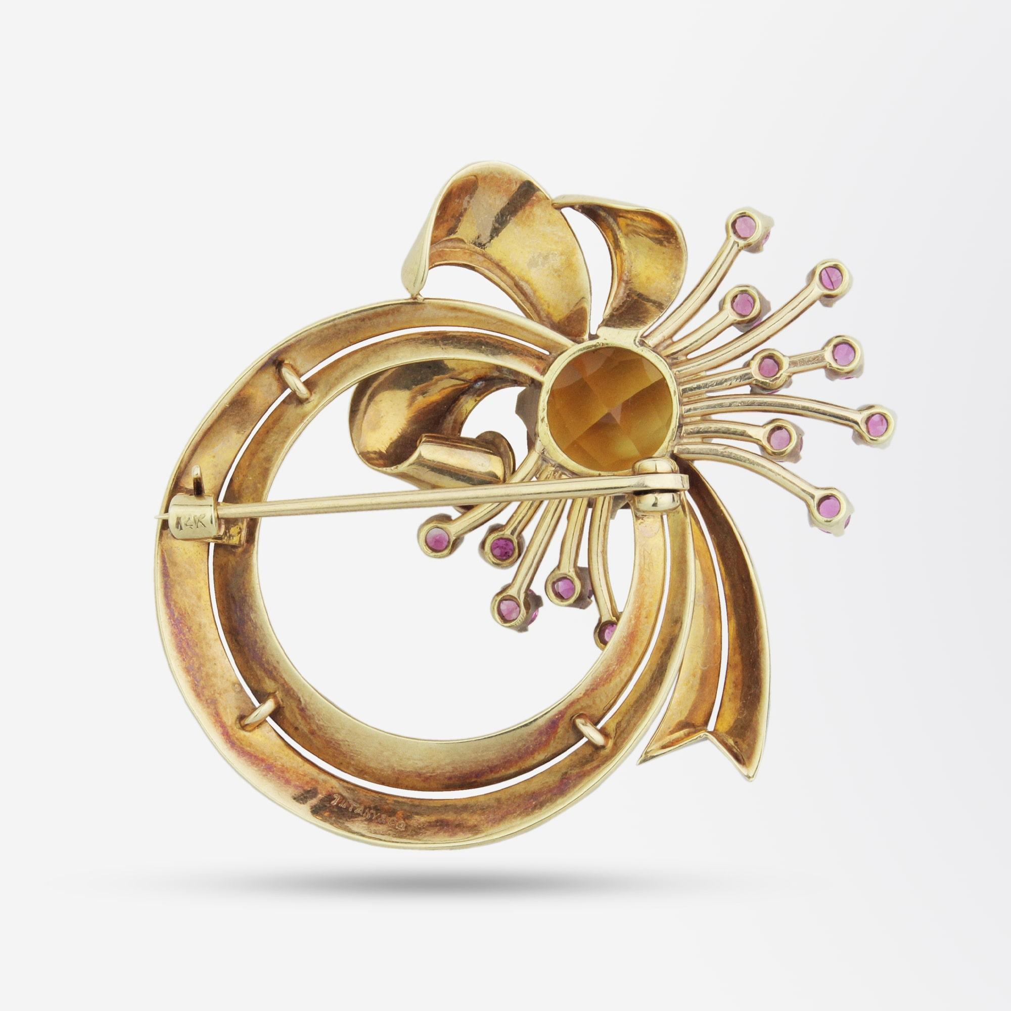 A mid-century, retro period, 14 karat yellow gold brooch by Tiffany & Company. The cocktail pin features a cushion cut citrine and 13 round mixed cut pink sapphires which combined with the sculpted gold 'ribbon' create a 'spray' of colour, often