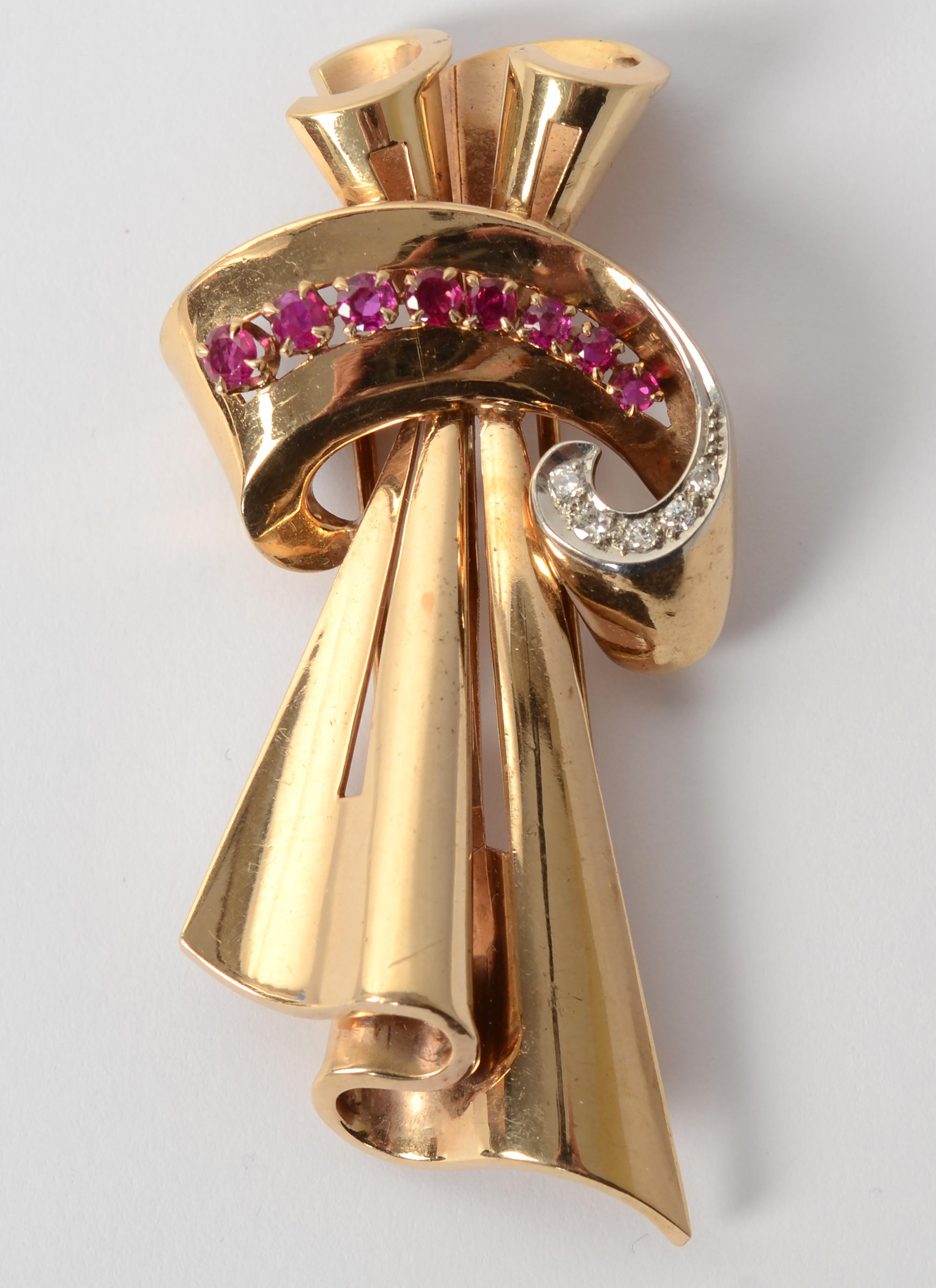 This scrolling gold, diamond and ruby brooch by Tiffany is the epitome of Retro design. Two draped lengthwise loops of gold give the appearance of fabric. Scrolling across the front is a gracefully curved band of gold on which are nine graduated