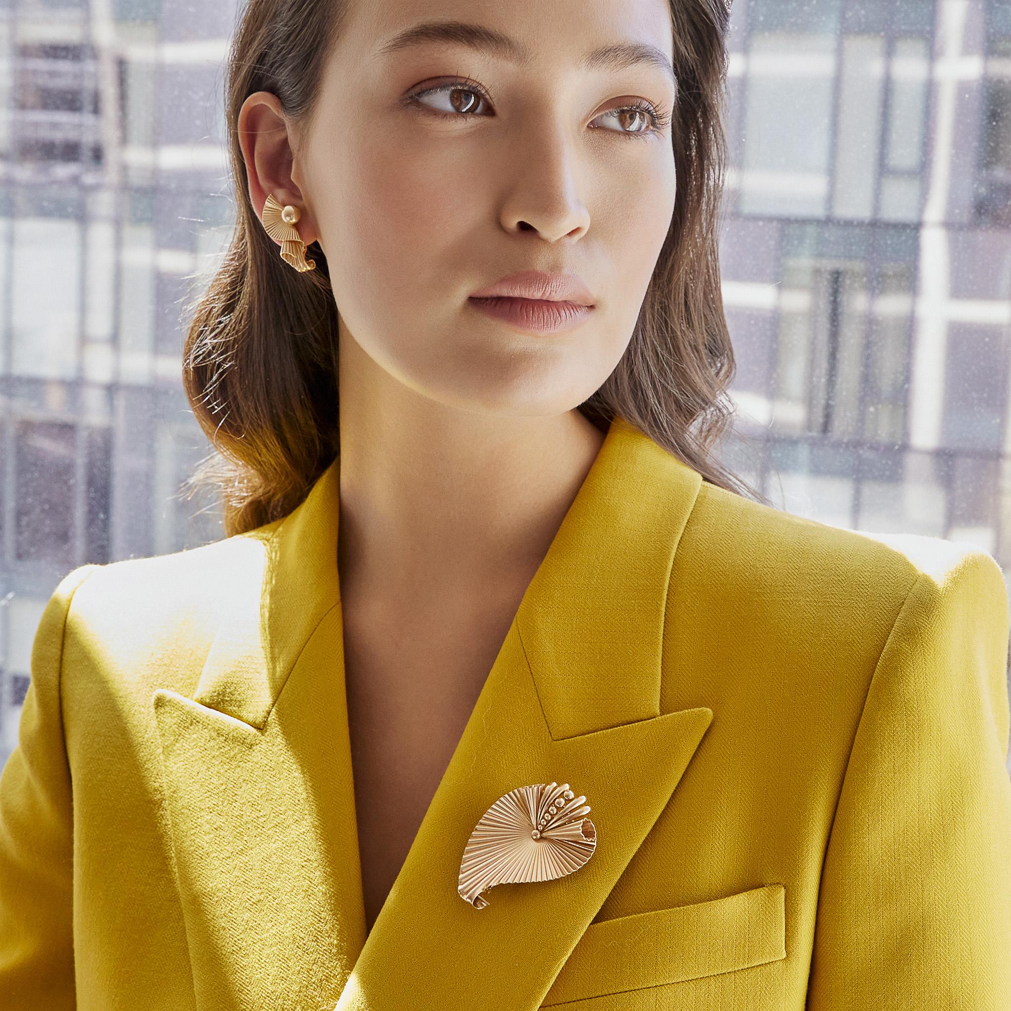 These Retro clip earrings and brooch are composed of 14K gold. The clip earrings are designed as ridged ribbons suspended from a domed ball top curling back upon themselves, while the brooch is a ribbed, scrolling leaf topped by volutes and a