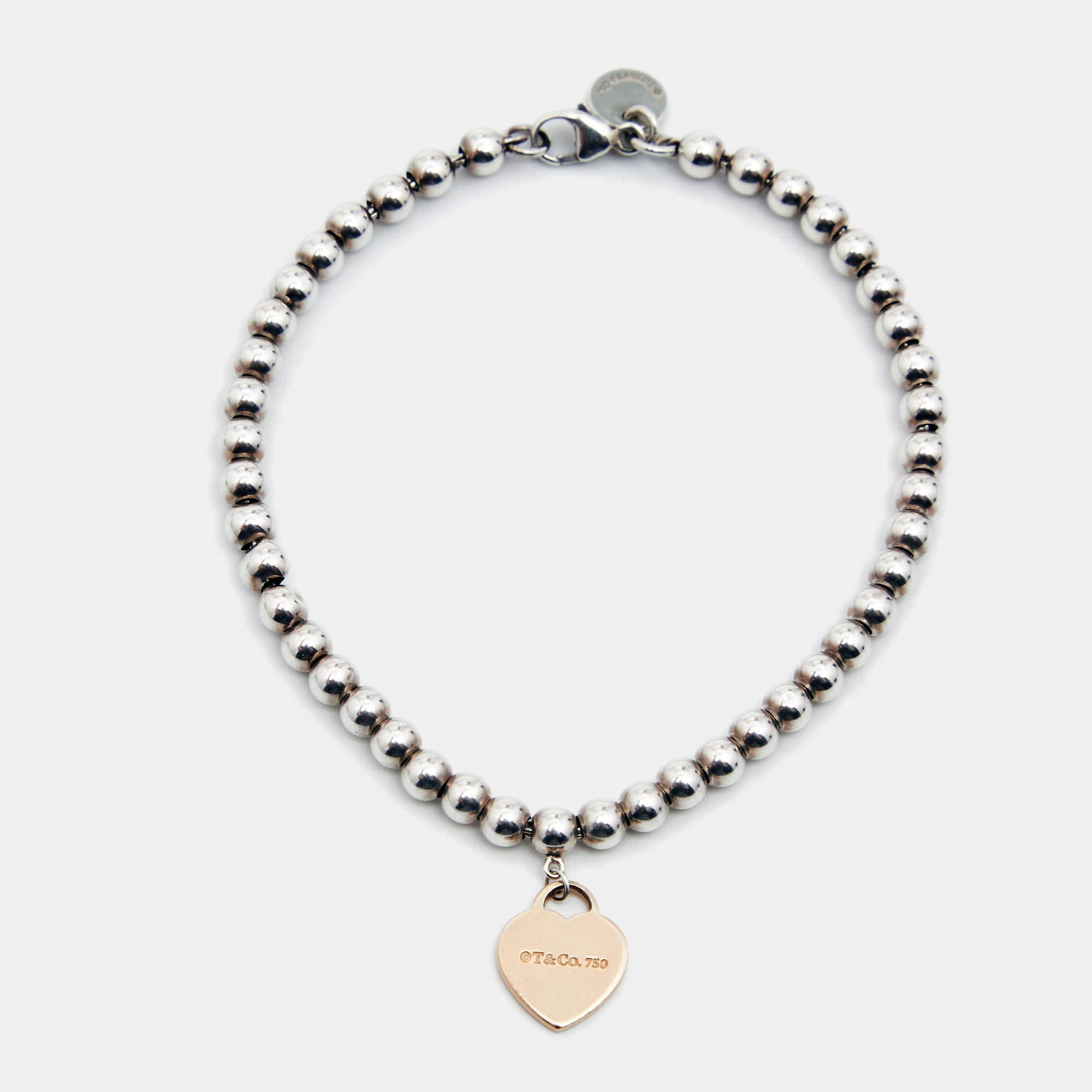 This Tiffany & Co. silver bracelet is from the famous collection titled Return To Tiffany. Crafted from sterling silver, the elegant piece carries an 18k rose gold heart pendant with engravings on the back and a bead bracelet with a lobster clasp.