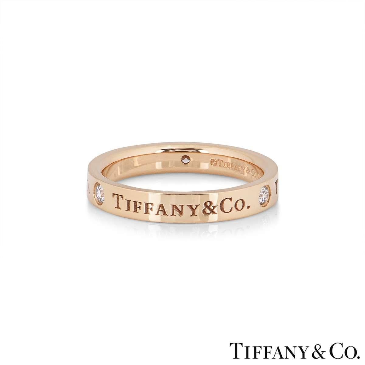 An 18k rose gold Tiffany & Co band ring. The ring features the Tiffany & Co. logo engraved around he outer edge, with 3 round brilliant cut diamonds set in-between. The diamonds have a total carat weight of 0.07ct. The ring measures 3mm in width and