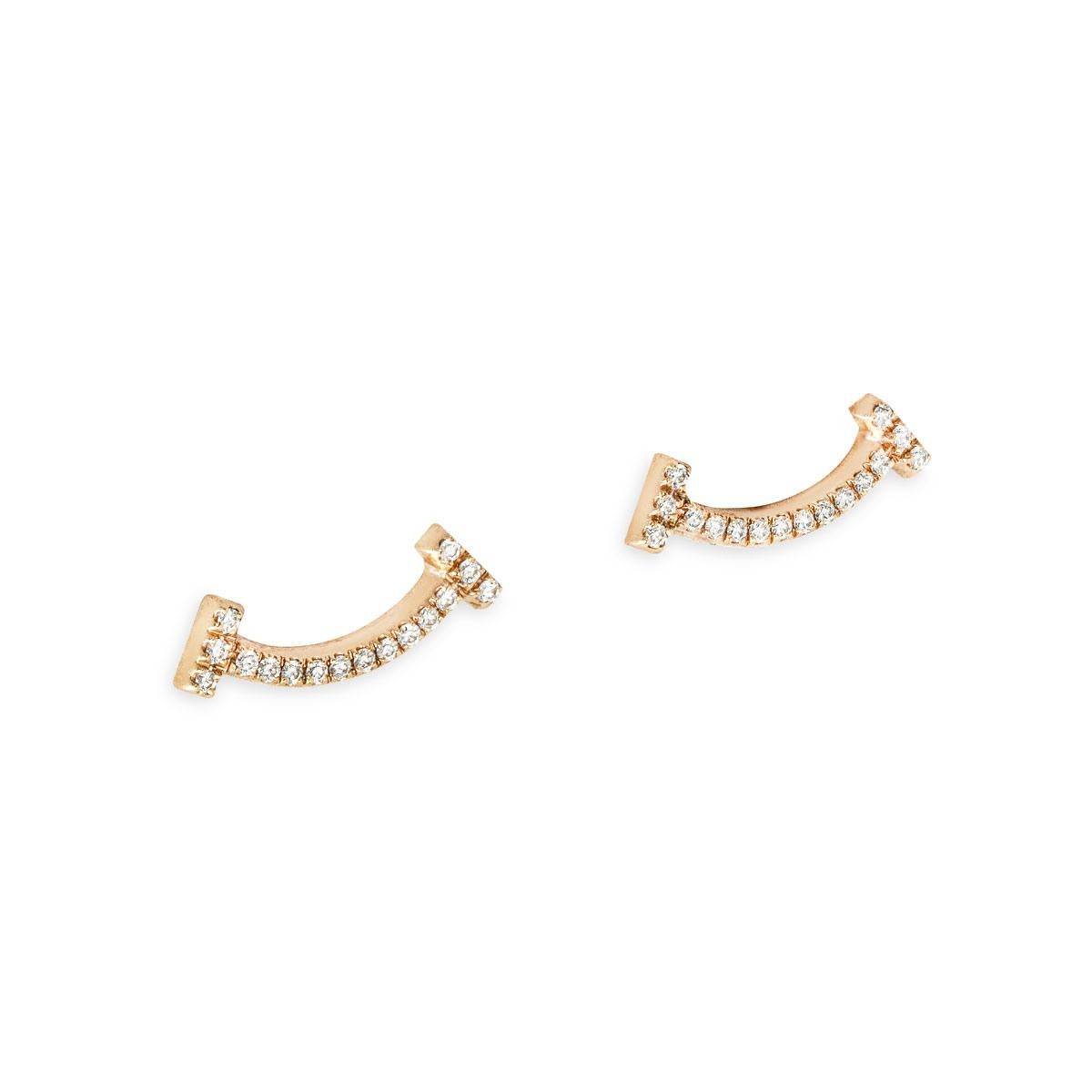 Un affascinante paio di orecchini di diamanti Tiffany & Co. in oro rosa 18 carati della collezione Tiffany T Smile. Gli orecchini sono composti da un motivo a sorriso con diamanti rotondi taglio brillante per un peso totale di 0,06 carati. Sono