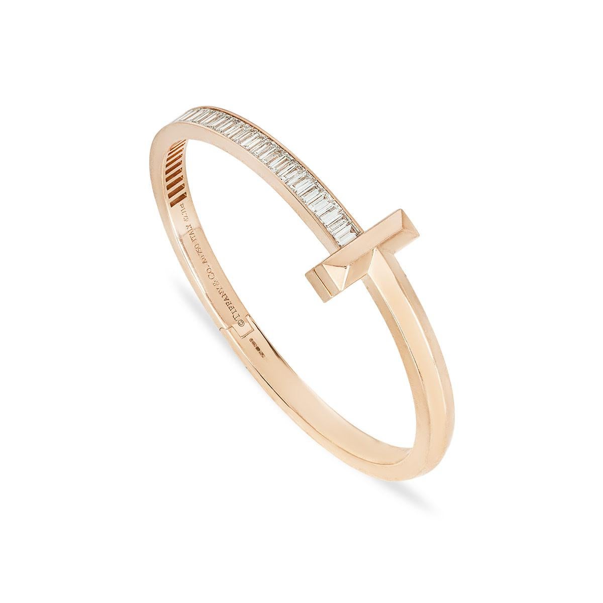 An extravagant 18k rose gold diamond bracelet by Tiffany & Co. from the Tiffany T collection. The bracelet wraps around the wrist with the iconic Tiffany T motif at the centre. The 32 baguette cut diamonds are pave set along the top of the bangle,