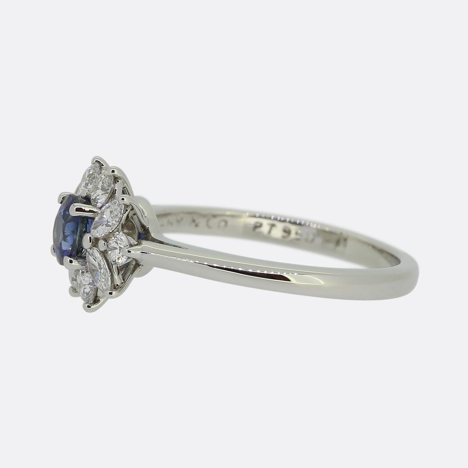 Ecco un anello a grappolo splendidamente realizzato dai famosi designer di gioielli Tiffany & Co. Al centro si trova uno zaffiro rotondo sfaccettato con una tonalità di colore blu fiordaliso meravigliosamente iridescente. Questa pietra principale è